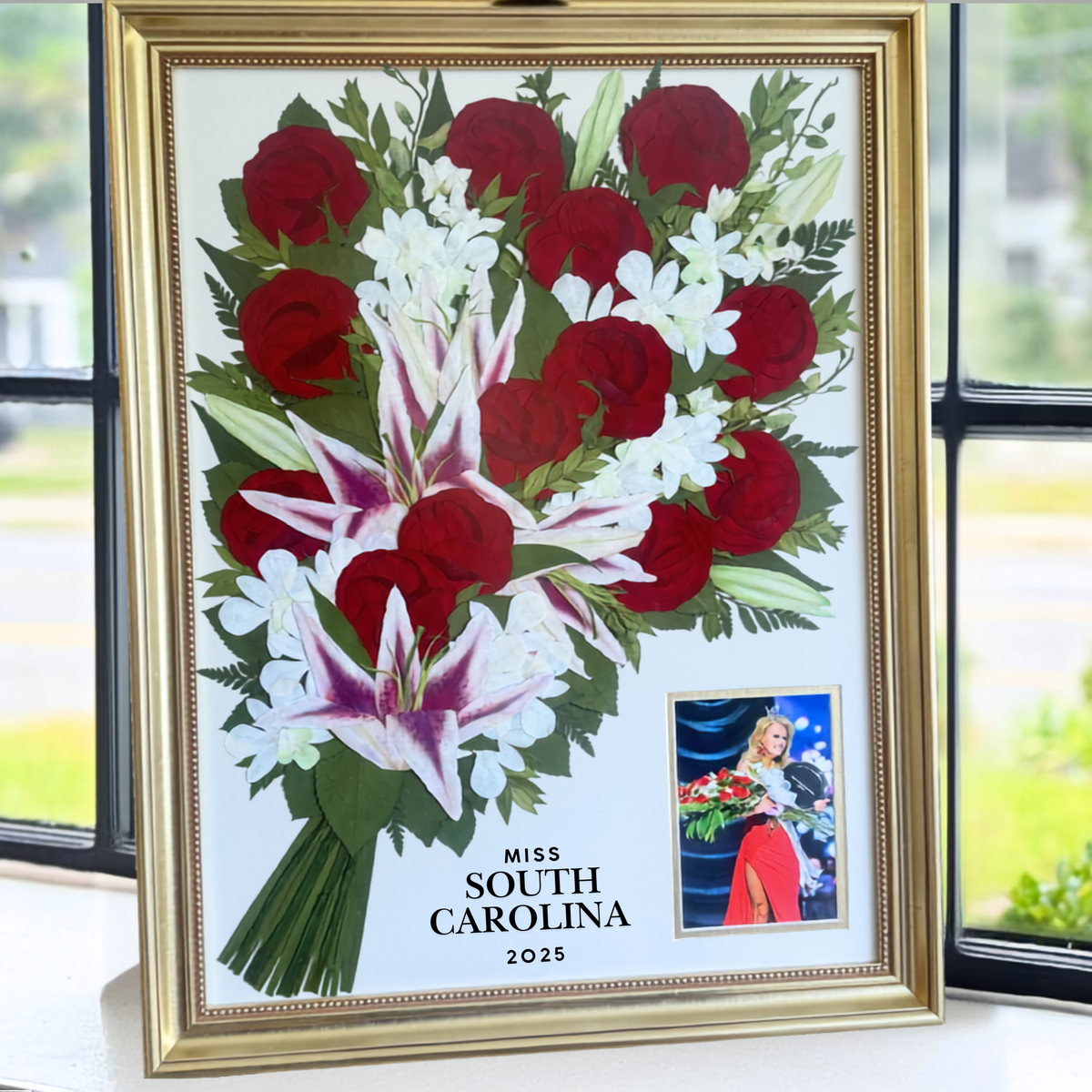 18x24 pressed flower bouquet preservation featuring red roses, stargazer lilies, and white flowers displayed in a gold frame with a Miss South Carolina 2025 photograph.