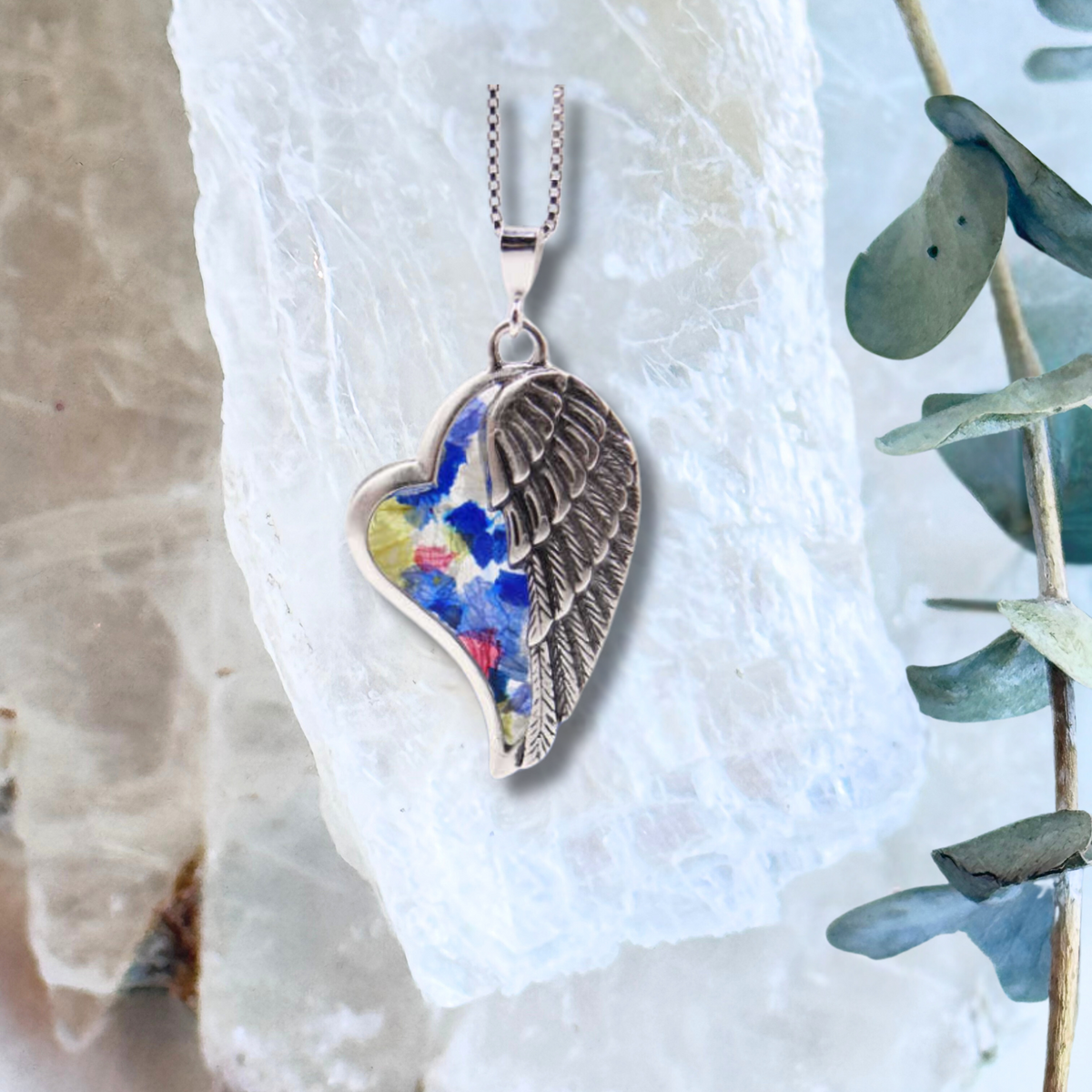 Angel&#39;s Embrace Pendant with preserved flowers, featuring a sterling silver heart wrapped in a delicate angel wing.