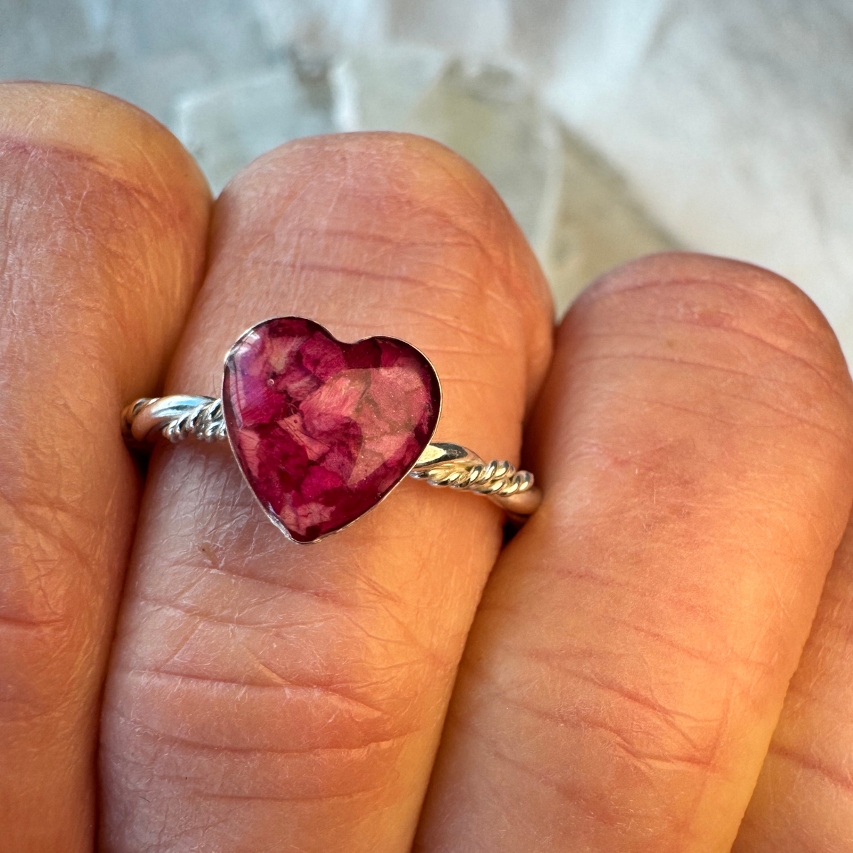 Beloved Heart Keepsake Ring worn on finger, featuring an 8mm heart-shaped setting handcrafted from preserved flowers in sterling silver.