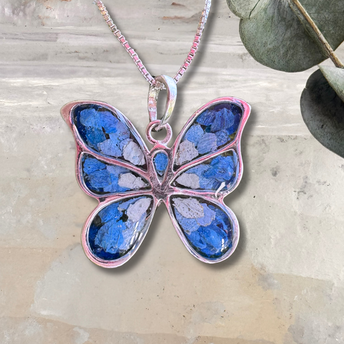 Handcrafted butterfly-shaped pendant featuring preserved blue funeral flowers, symbolizing remembrance and transformation.