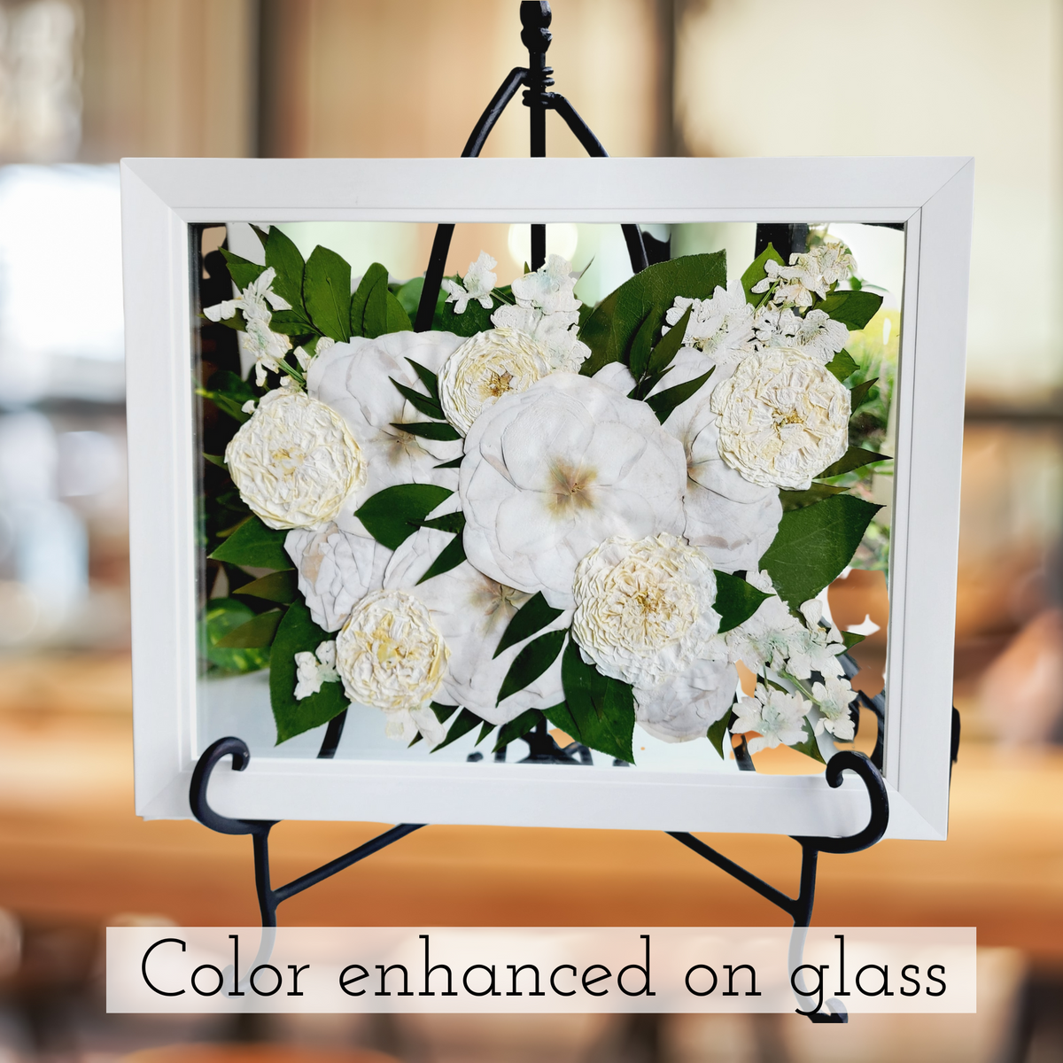 Color-enhanced 11x14 floating pressed flower art on glass with white roses and greenery in white frame, displayed on black stand