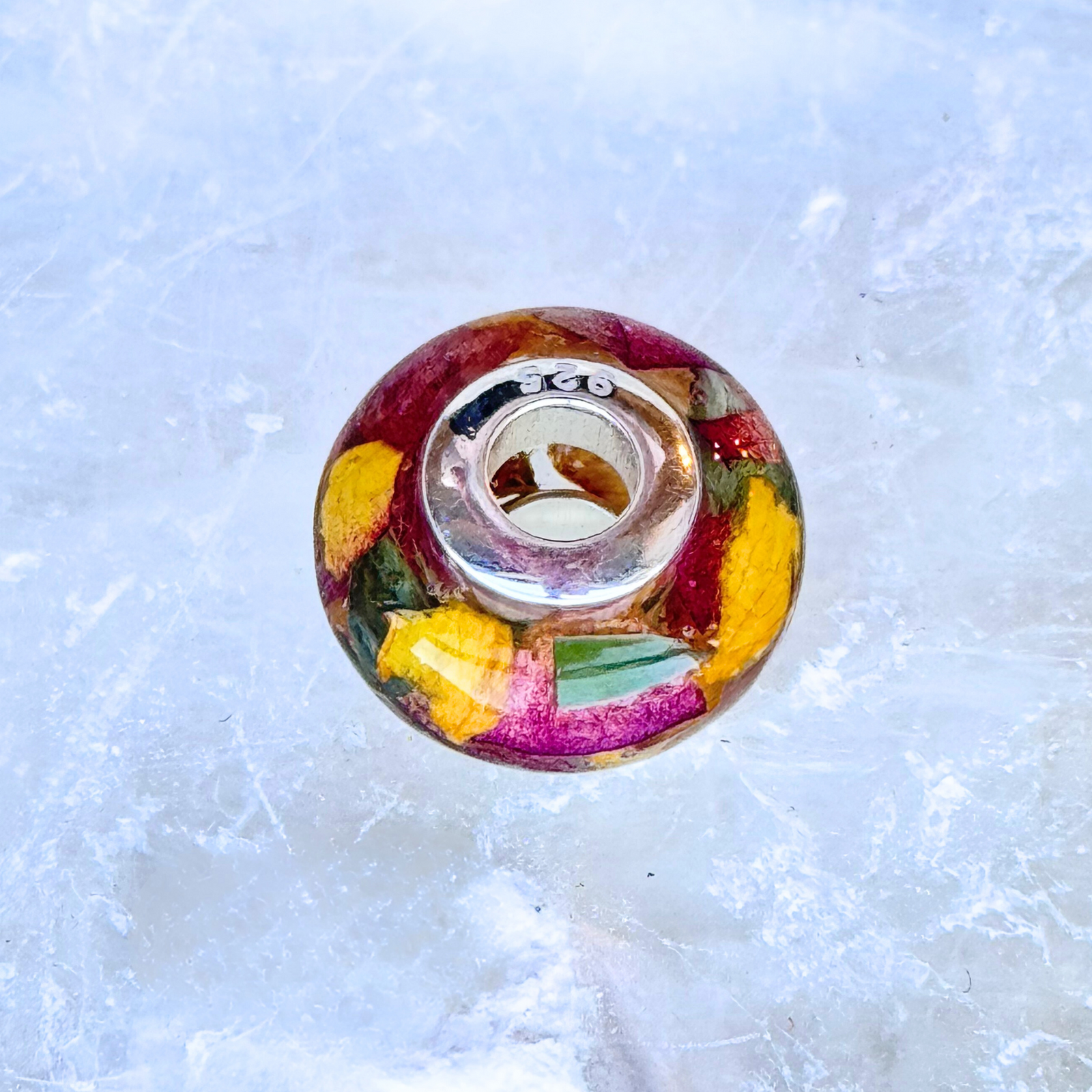 Detailed view of a round charm bead made with preserved red, yellow, and green flower petals in resin, featuring a 925 sterling silver core. Fits most European-style bracelets and serves as a beautiful memorial keepsake.