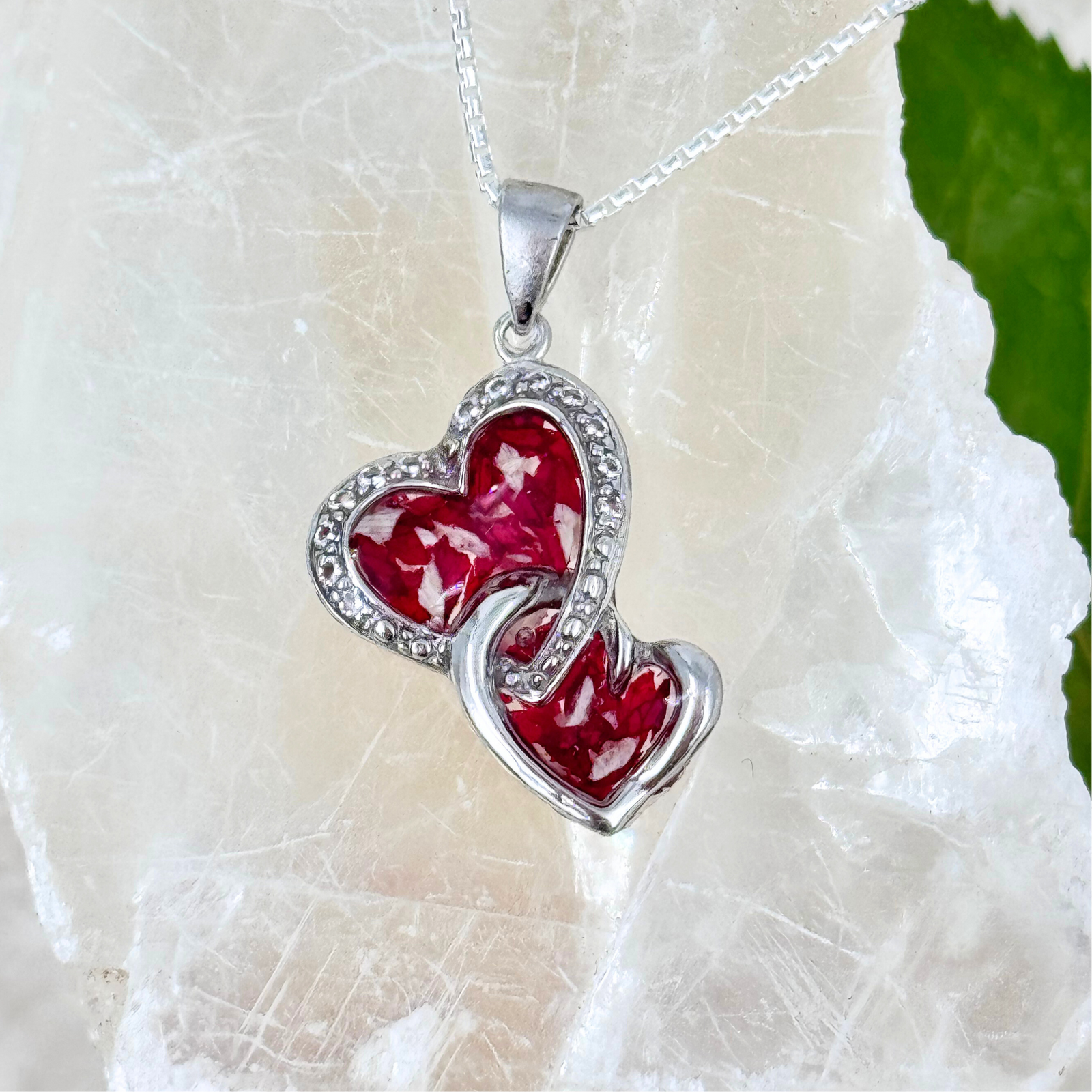 Main image of a sterling silver double heart pendant filled with deep red preserved flower petals in clear resin, accented with delicate crystal details. A handcrafted memorial necklace designed to honor the memory of a loved one.