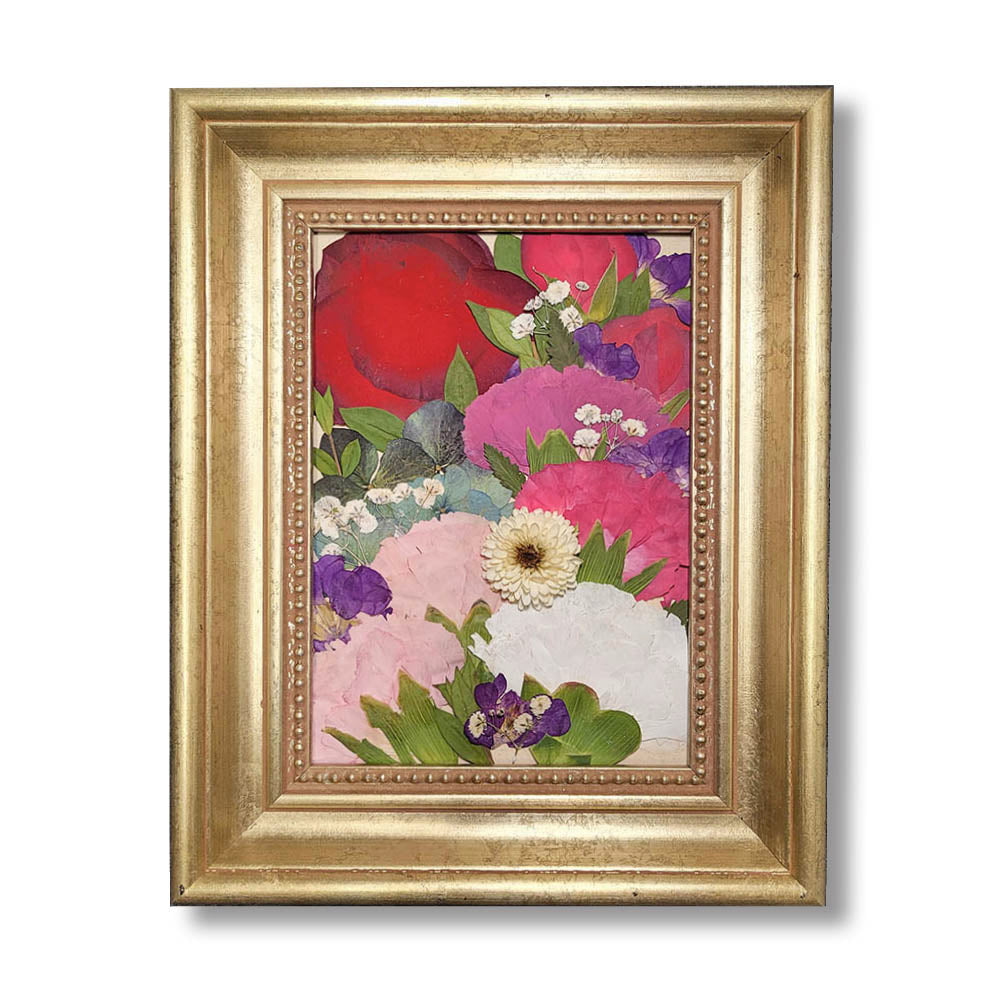 A 5 × 7 pressed flower arrangement in a classic gold frame featuring layers of red, pink, white, purple, and ivory blooms accented with greenery and baby&#39;s breath. This vibrant floral collage preserves the beauty of a wedding bouquet or a memorial arrangement in timeless elegance.