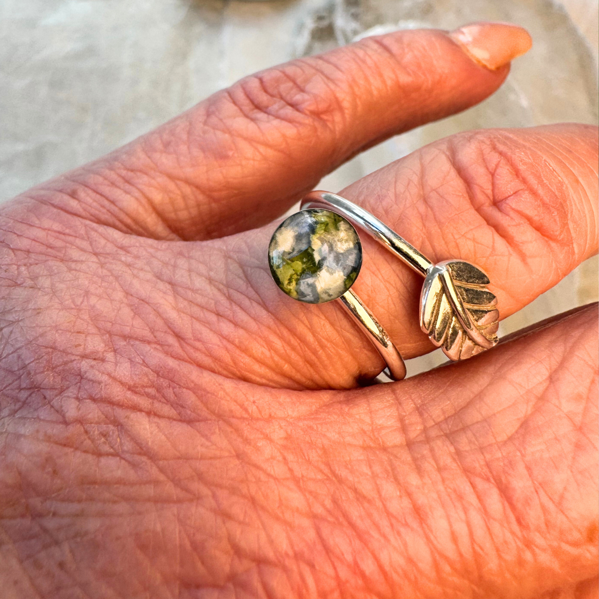 Everleaf Keepsake Ring shown worn on the hand, featuring an 8mm keepsake setting with preserved green, white, and blue flower petals. This sterling silver flower preservation ring can be handcrafted using wedding flowers, funeral flowers, cremation ashes, or pet fur.