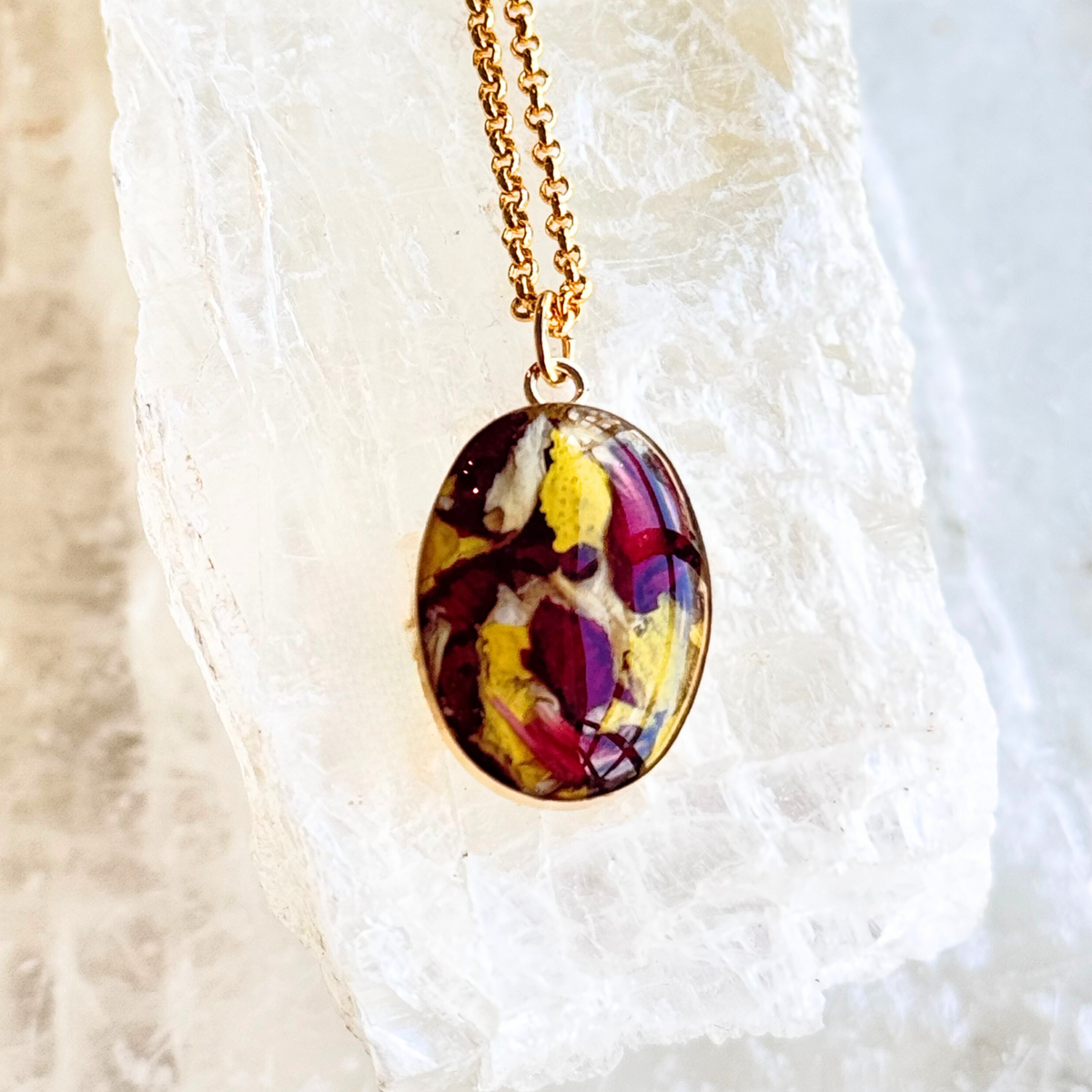 A gold-filled oval memorial pendant featuring a custom floral inlay with preserved red and yellow roses, honoring cherished memories.