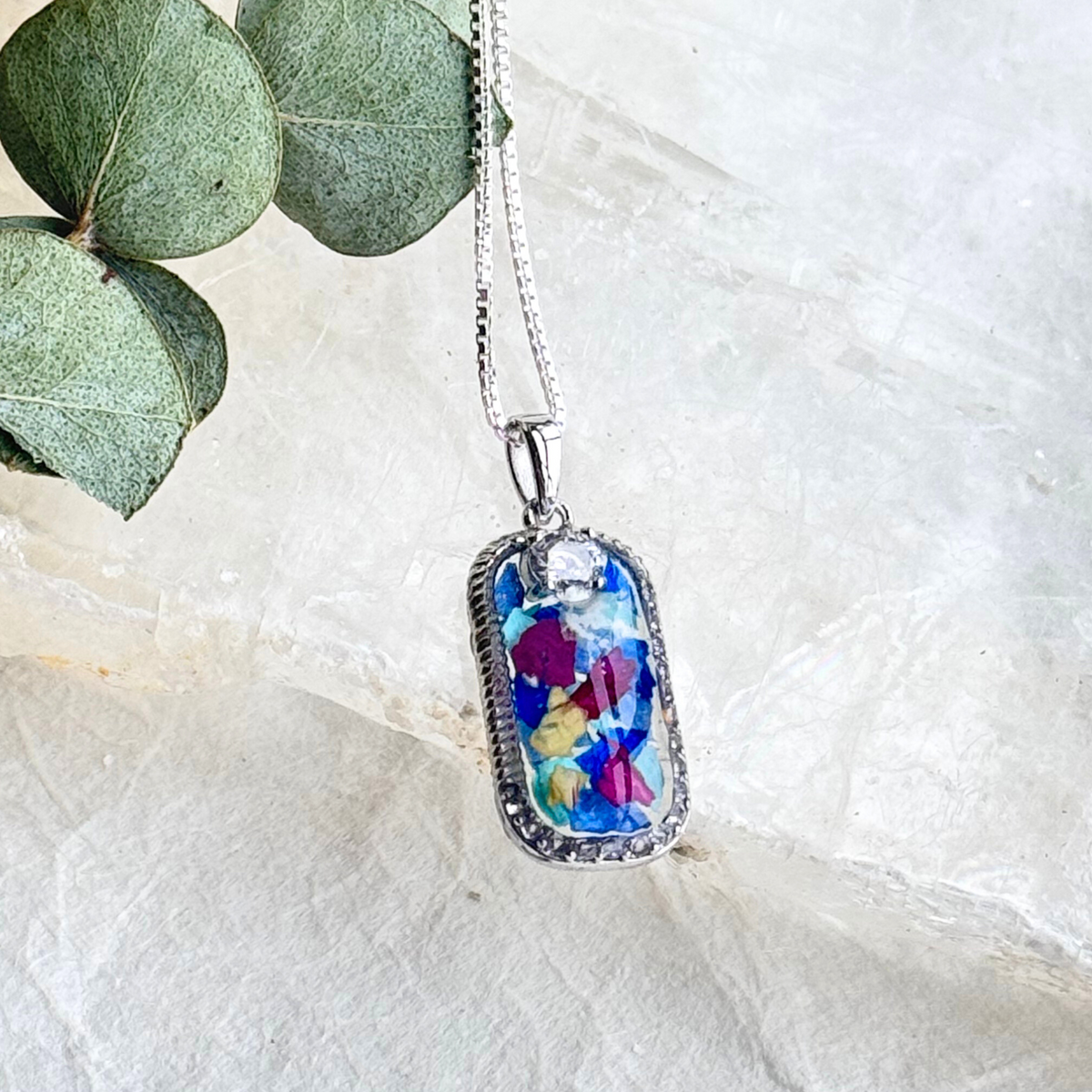 Artistic view of the Graceful Remembrance Pendant highlighting preserved flowers and elegant CZ details in a sterling silver rectangular design.