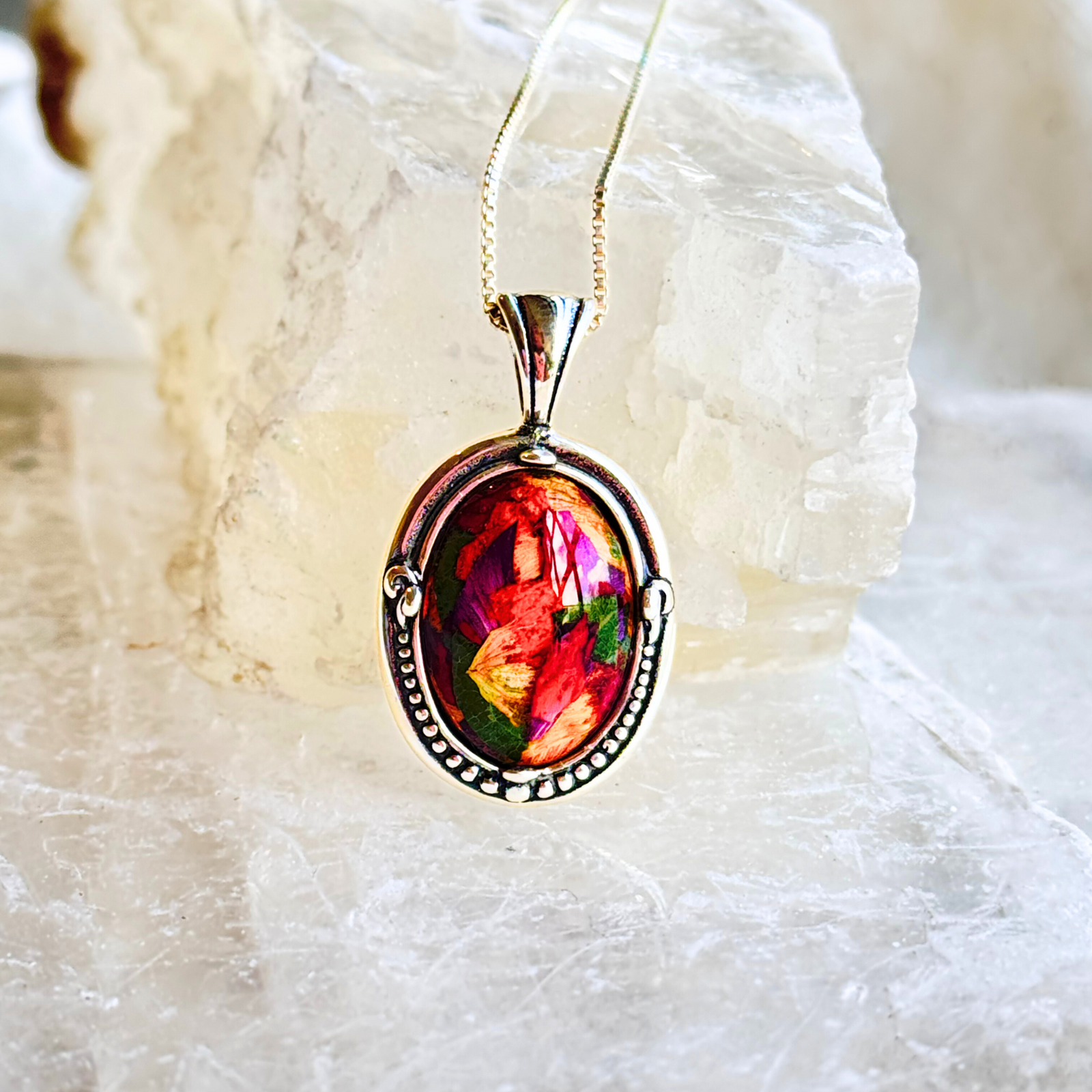 A sterling silver oval memorial pendant featuring a handmade floral inlay infused with preserved funeral flowers.