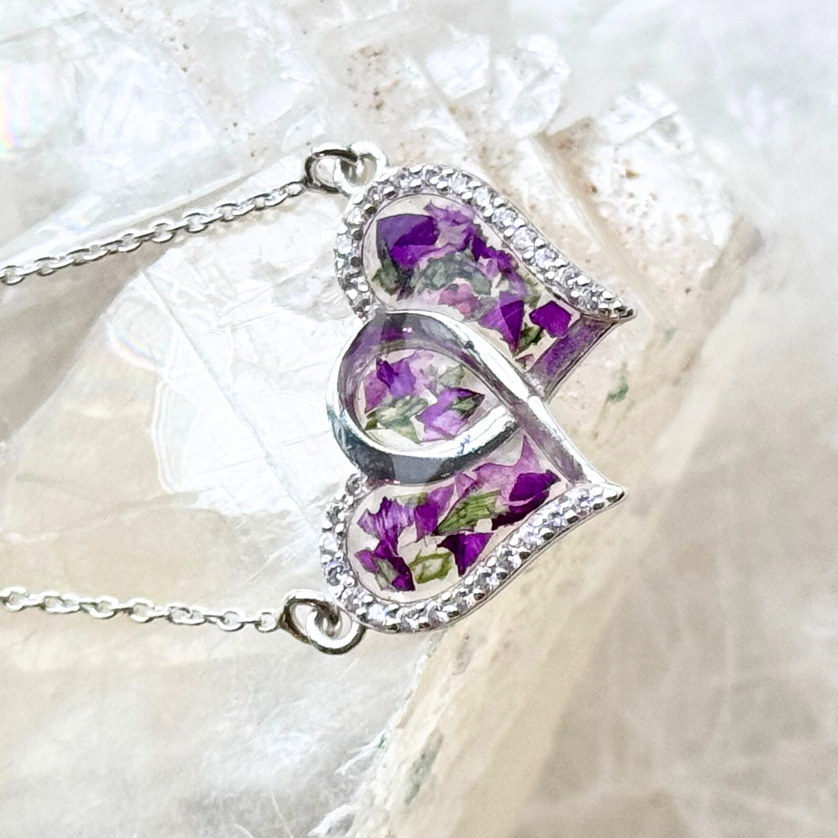  Artistic close-up of the Infinity Heart Pendant, highlighting the vibrant preserved flowers and delicate CZ accents in the intertwined heart design.