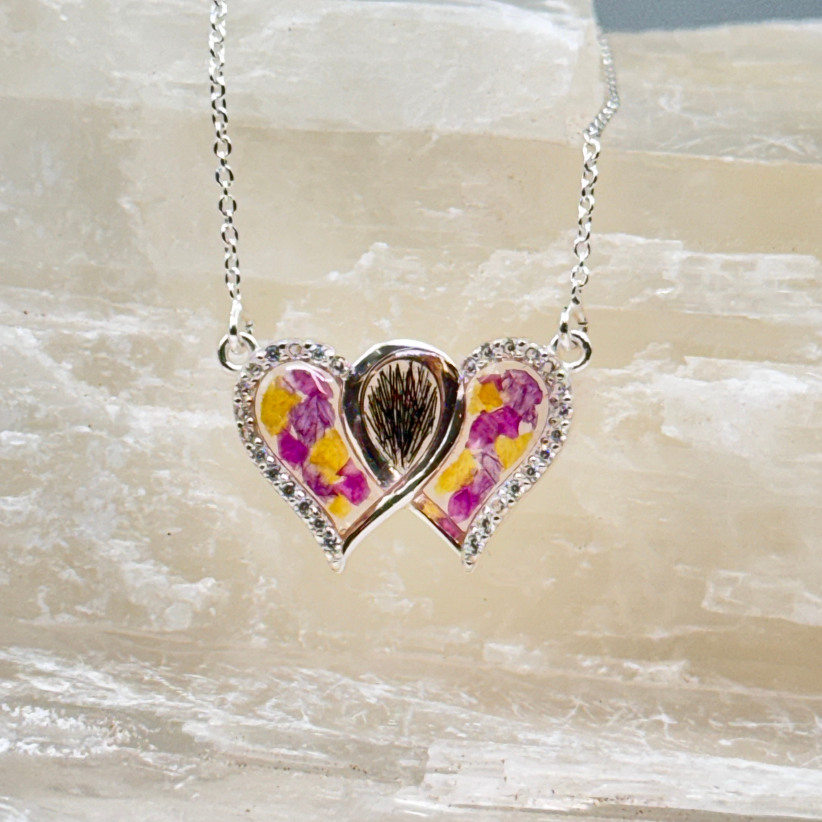 Infinity heart-shaped memorial pendant made with preserved hair and colorful pressed flowers in a silver setting.