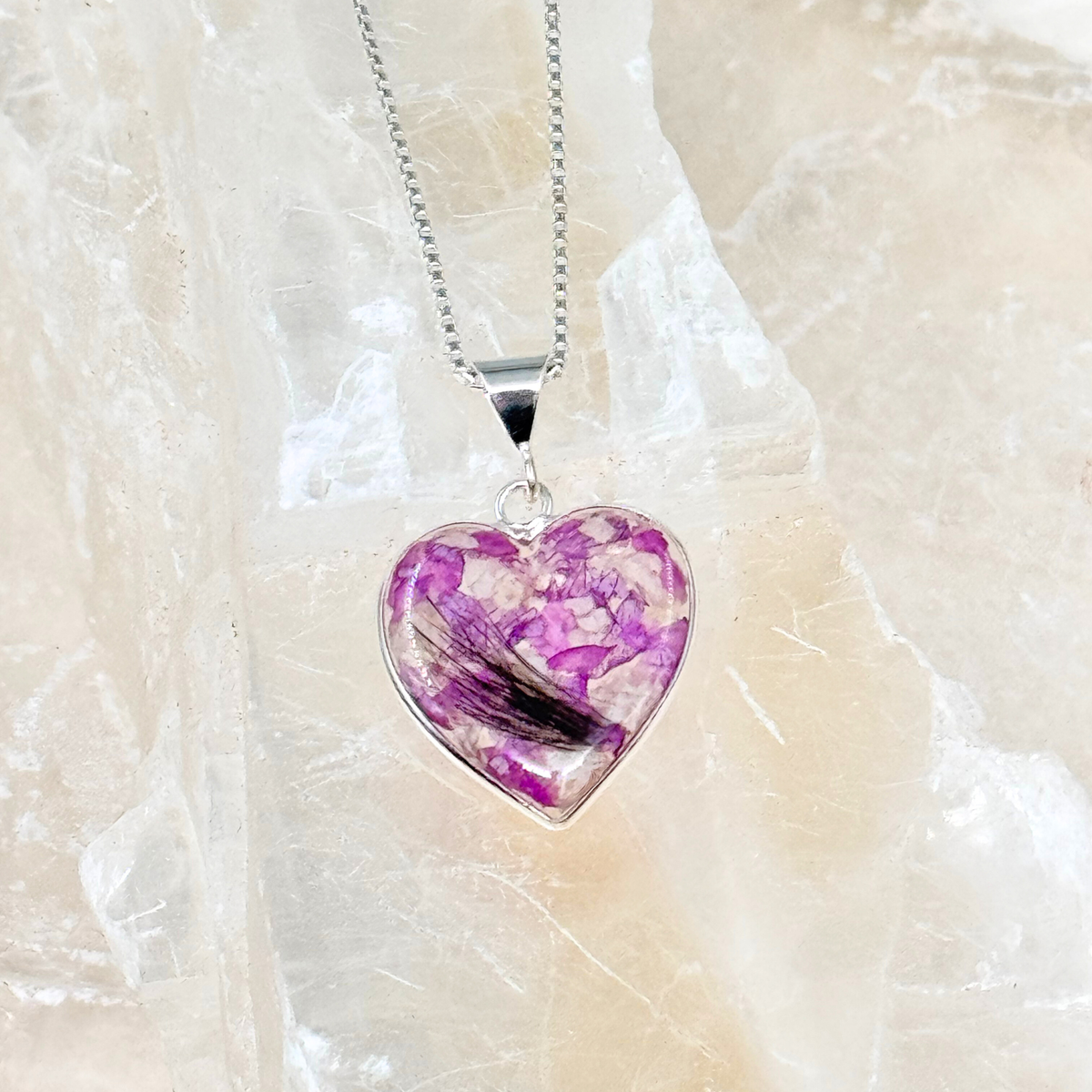 Heart-shaped memorial pendant made with purple flowers and a lock of pet hair, encased in clear resin on a silver chain.
