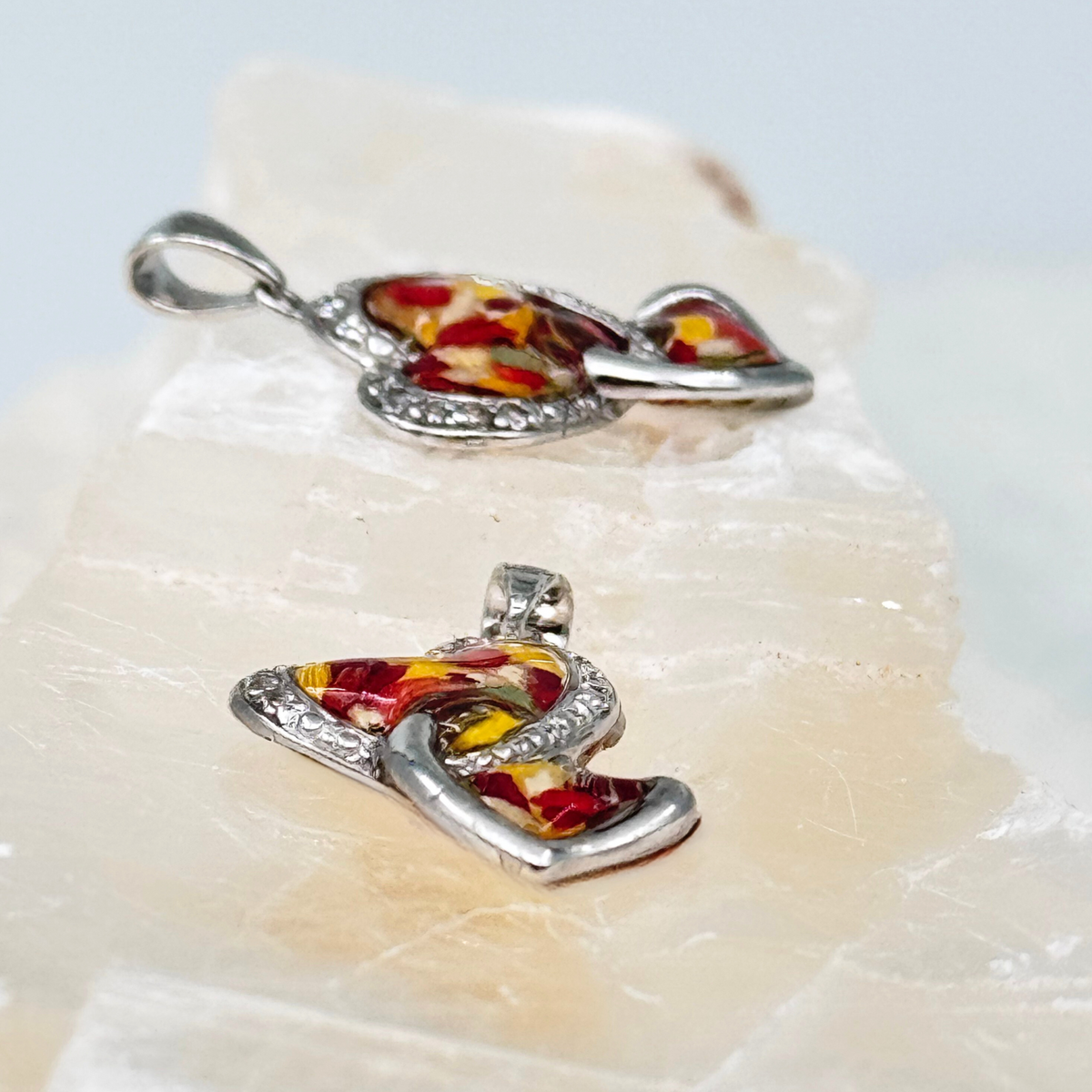 Sterling silver heart-shaped memorial pendants filled with preserved red and yellow flower petals in resin, accented with crystal detailing. A touching keepsake to honor a loved one’s memory.