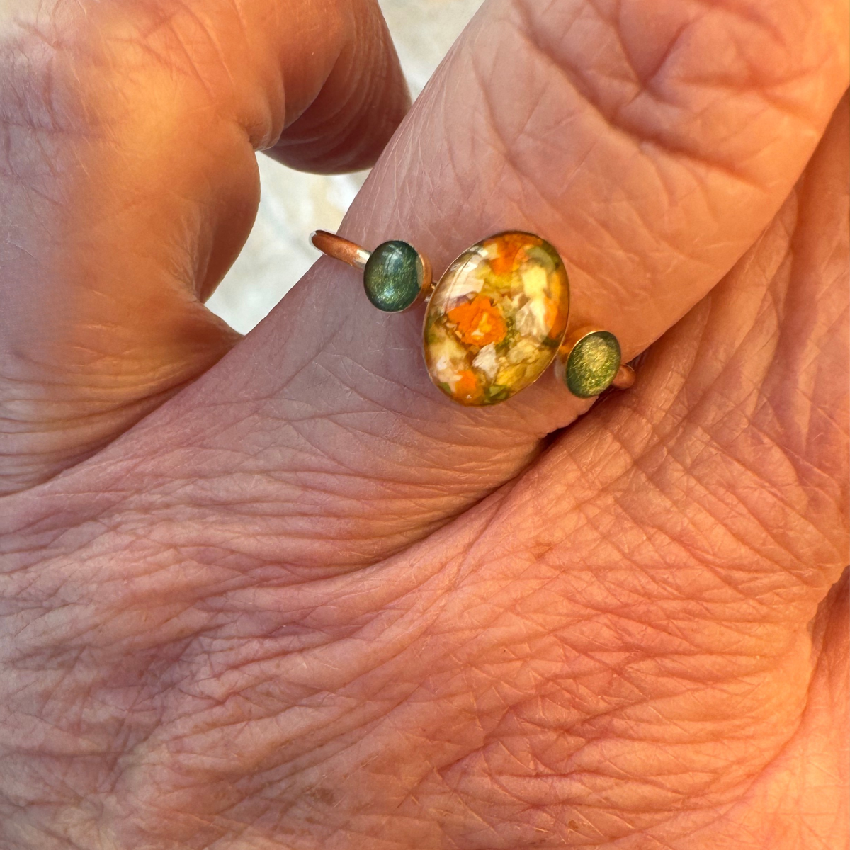 Close-up of the Meadowlight Keepsake Ring worn on a hand, featuring preserved flowers in an 8x10mm oval center setting and two 5mm memorial settings for cremation ashes, handcrafted in gold-plated sterling silver.