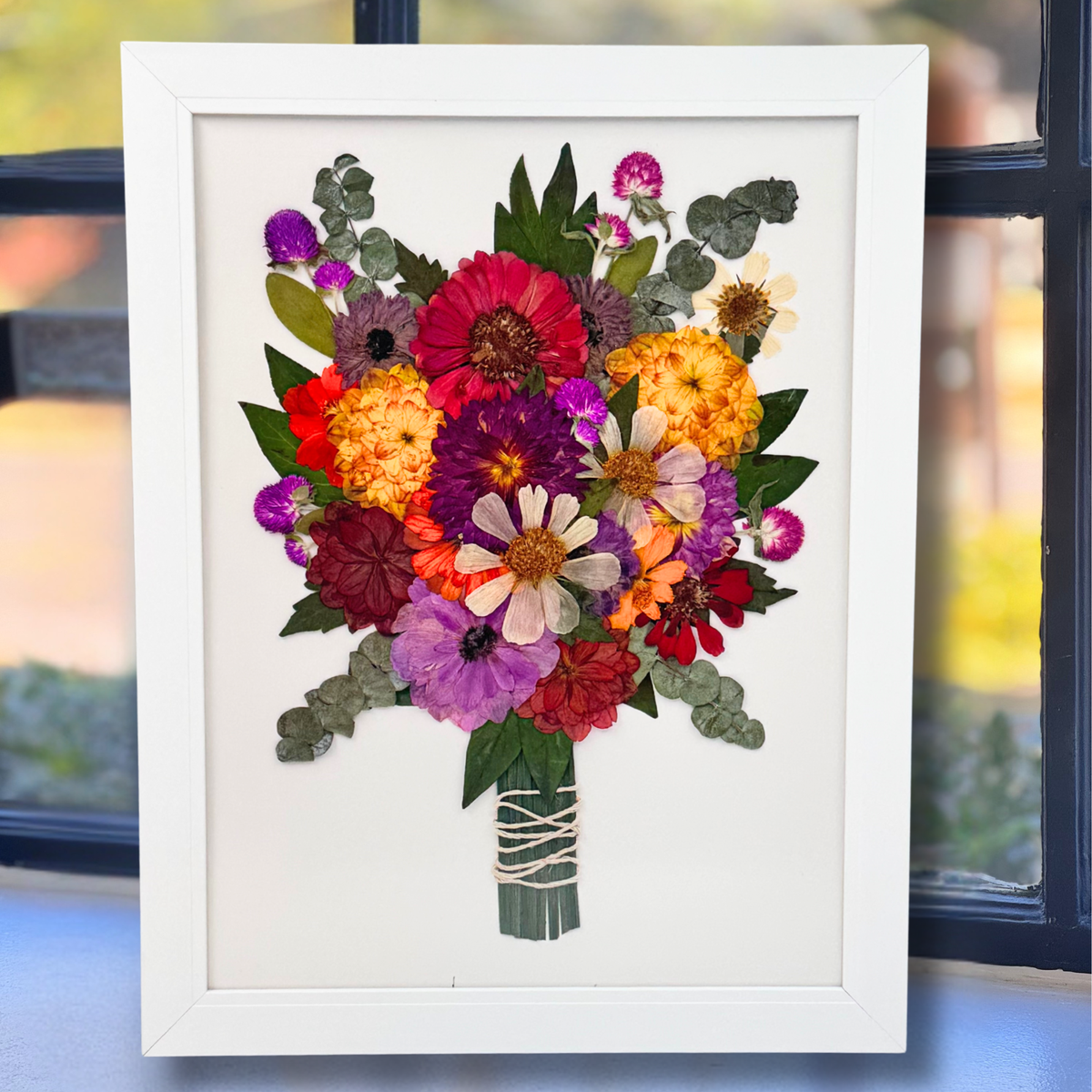 Colorful pressed flower wedding bouquet arranged in an 12x16 white frame with a clean white background, showcasing vibrant blooms like zinnias, eucalyptus, and gomphrena.