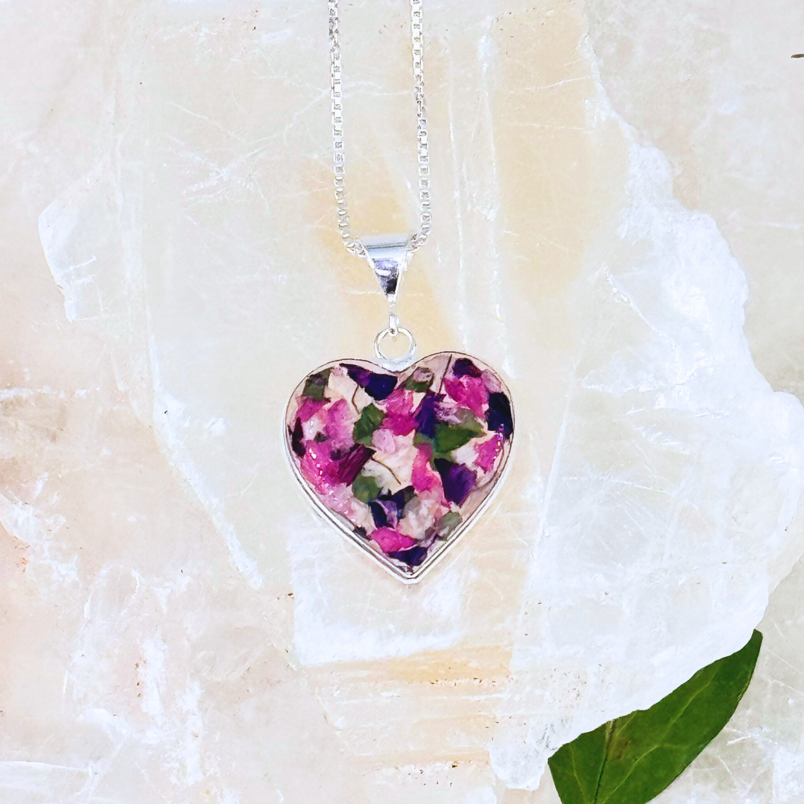 Handcrafted heart-shaped pendant featuring preserved dried flowers in resin, symbolizing remembrance and love. Set in silver with a delicate chain.