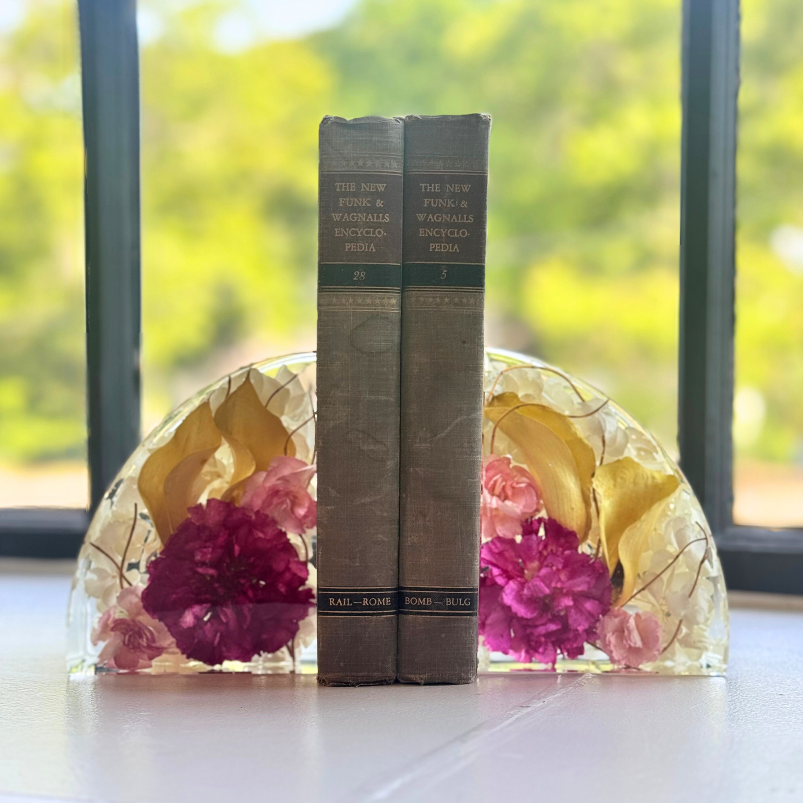 Two handcrafted resin bookends made with real yellow and pink flowers, holding books on a windowsill. A meaningful floral keepsake from funeral or wedding blooms.