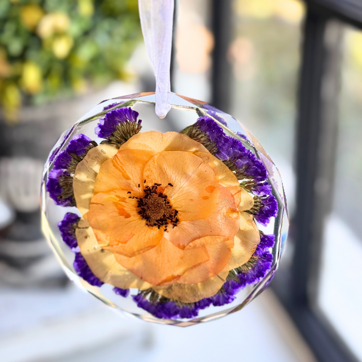 A handmade resin keepsake featuring a pressed rose and purple statice, displayed by a window to highlight its beauty in natural light.