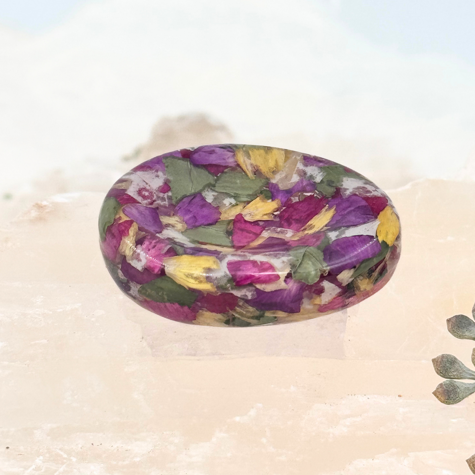 Oval resin worry stone filled with preserved pink, purple, yellow, and green flower petals, designed as a memorial keepsake or calming handheld token.