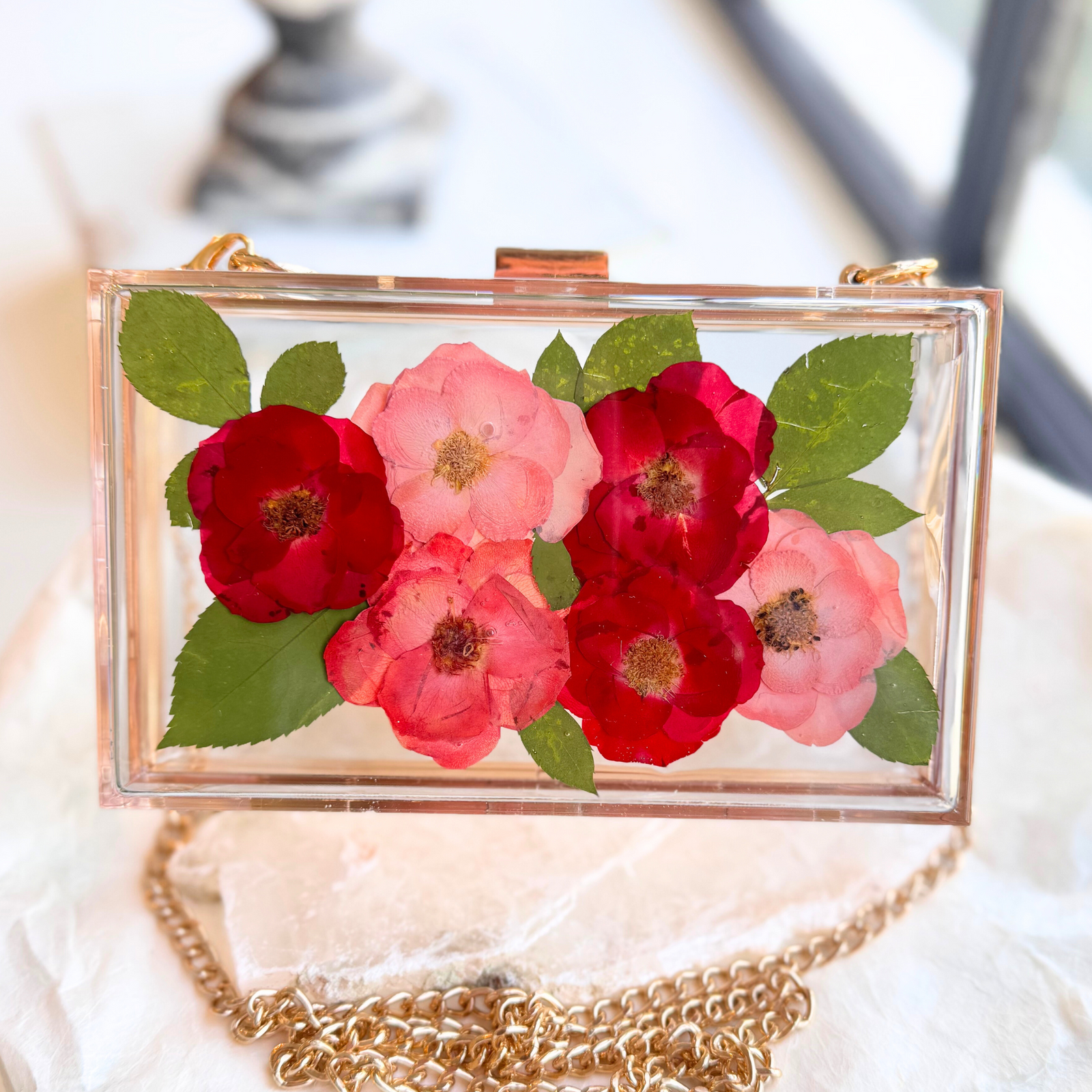 A handmade resin bridal clutch featuring pressed wedding flowers encased in clear acrylic, with a gold chain for elegant styling.