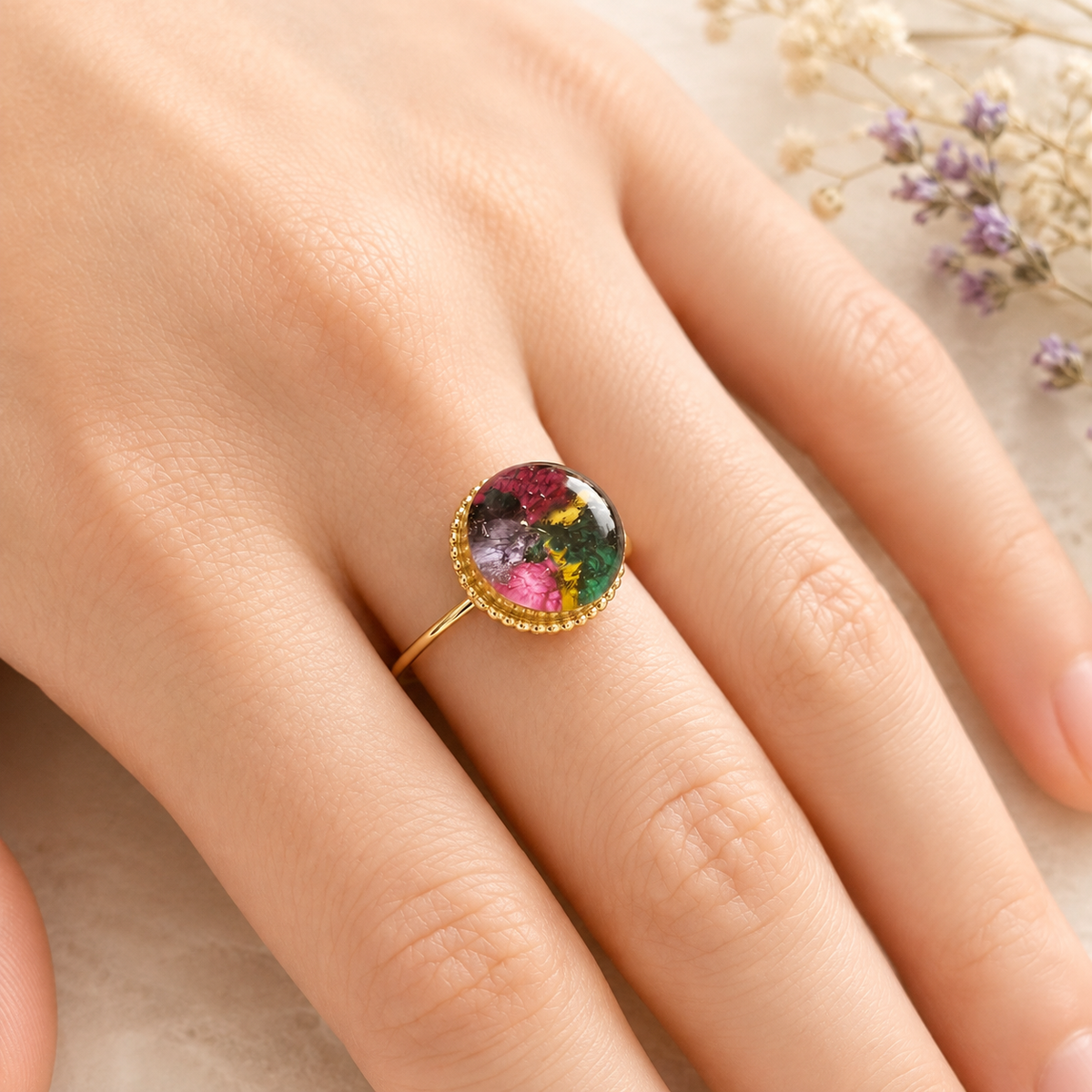 Model wearing Circle of Memories Ring with colorful preserved flowers in a gold setting.