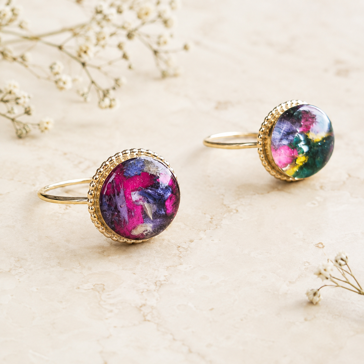 Two Circle of Memories Rings with colorful preserved flowers in gold settings.