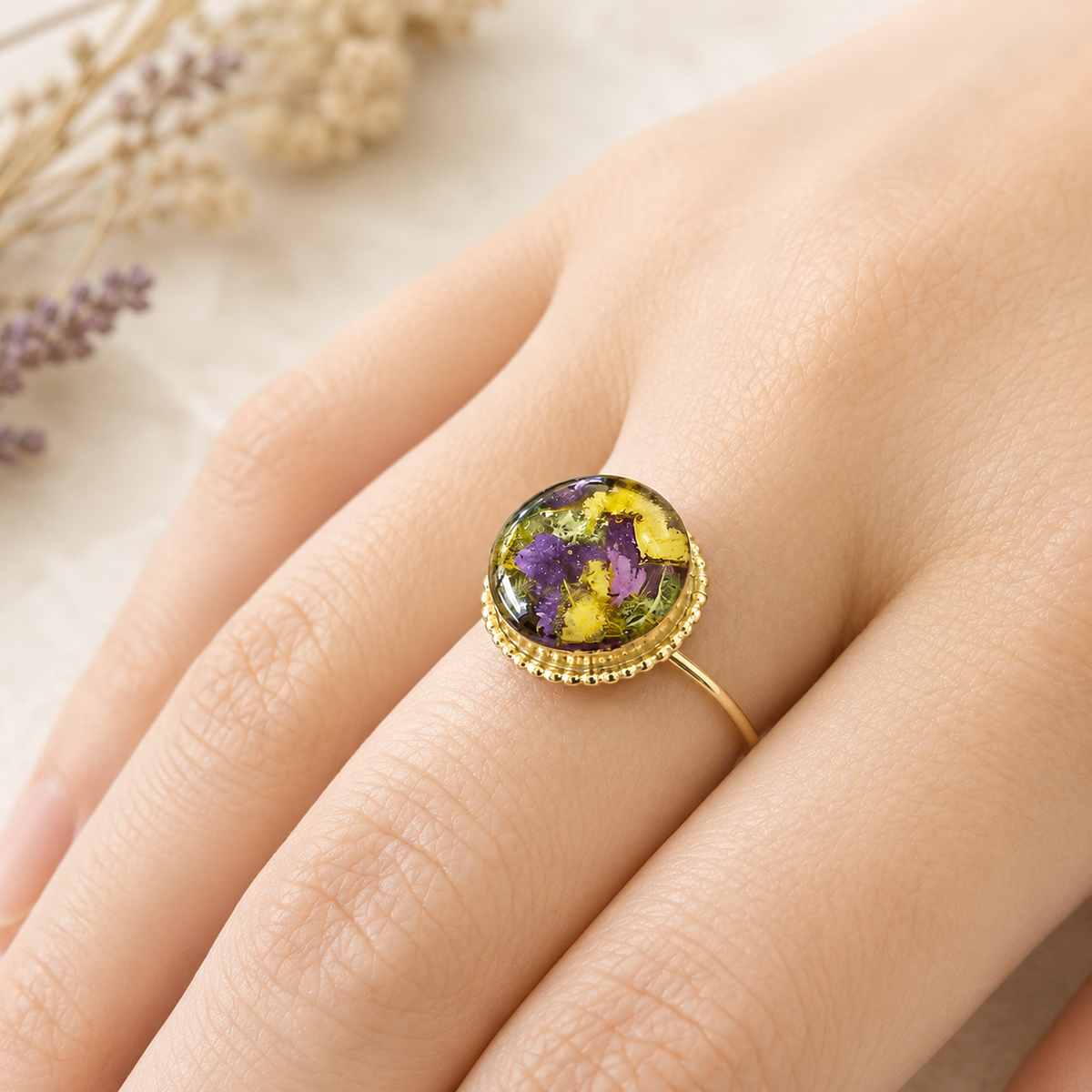 Model wearing Circle of Memories Ring with purple and yellow preserved flowers in a gold setting.