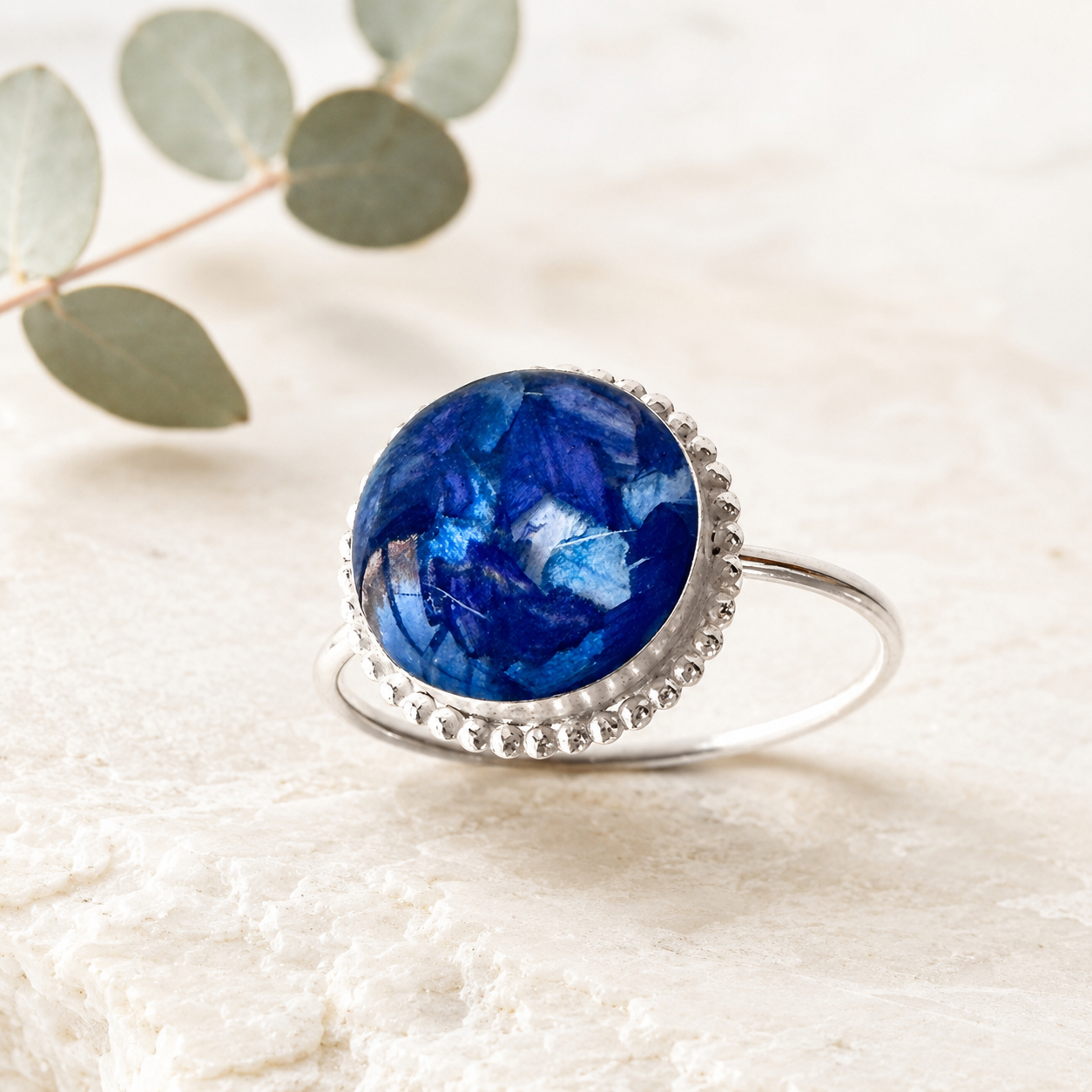 Close-up of blue preserved flowers in a silver memorial jewelry setting.