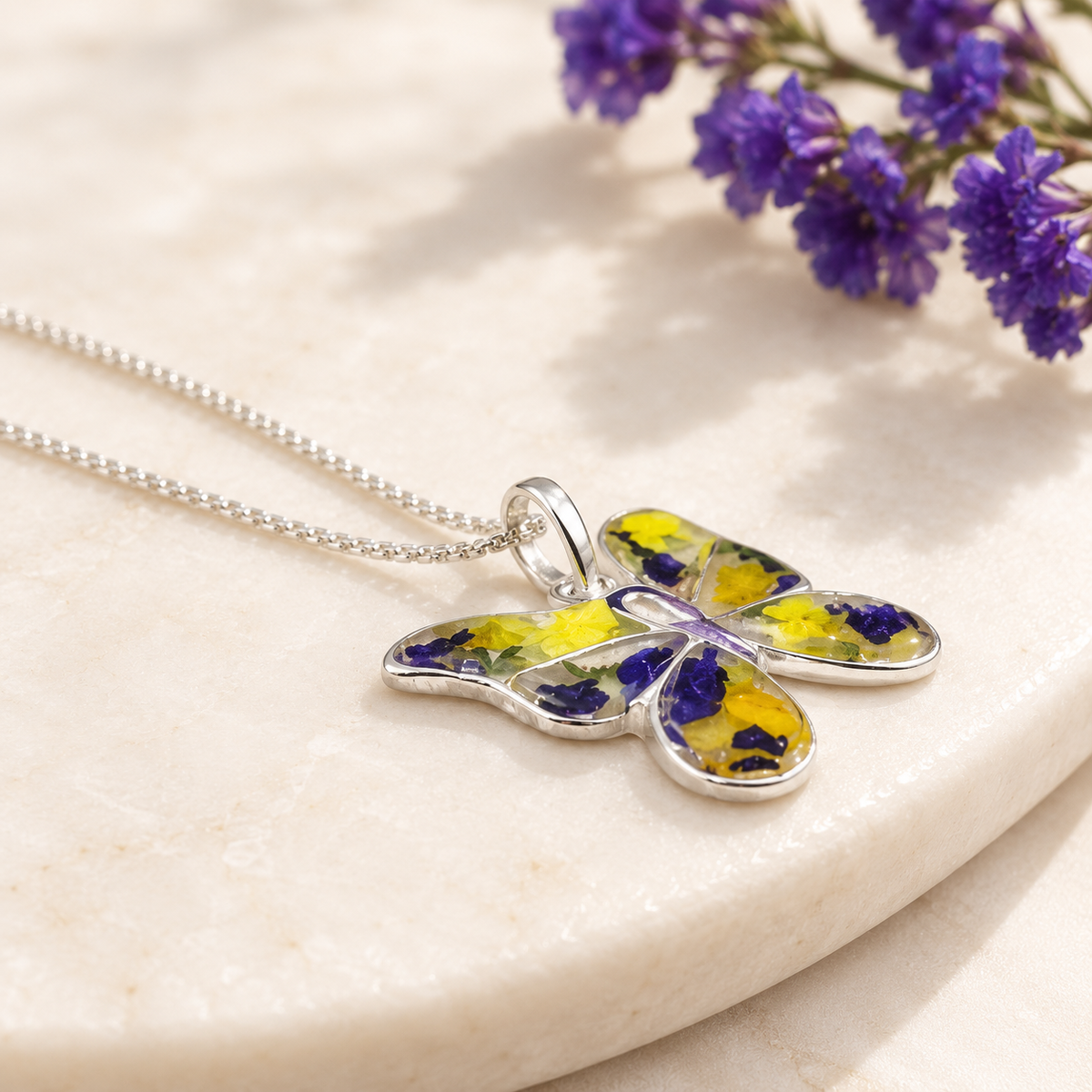Side view of a sterling silver butterfly keepsake pendant with yellow and blue preserved flowers.