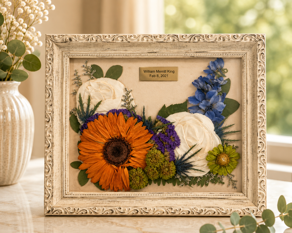Pressed orange, white and blue flowers with a memorial nameplate in an ornate 8x10 frame.