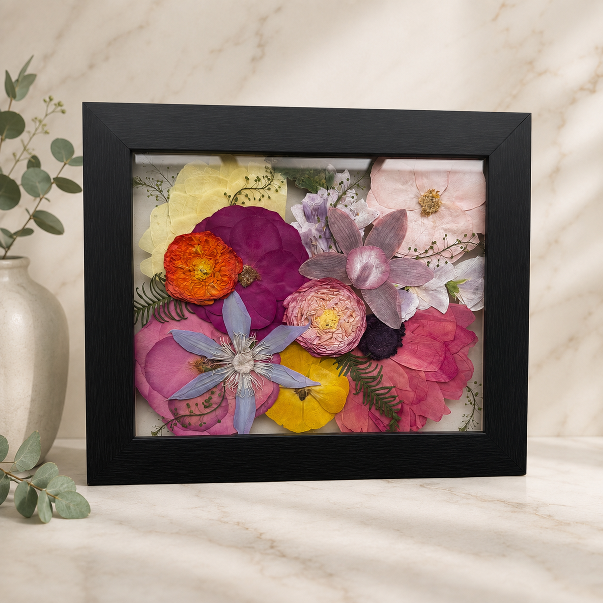 Pressed pink, purple, yellow and orange flowers preserved in a black 8x10 frame.