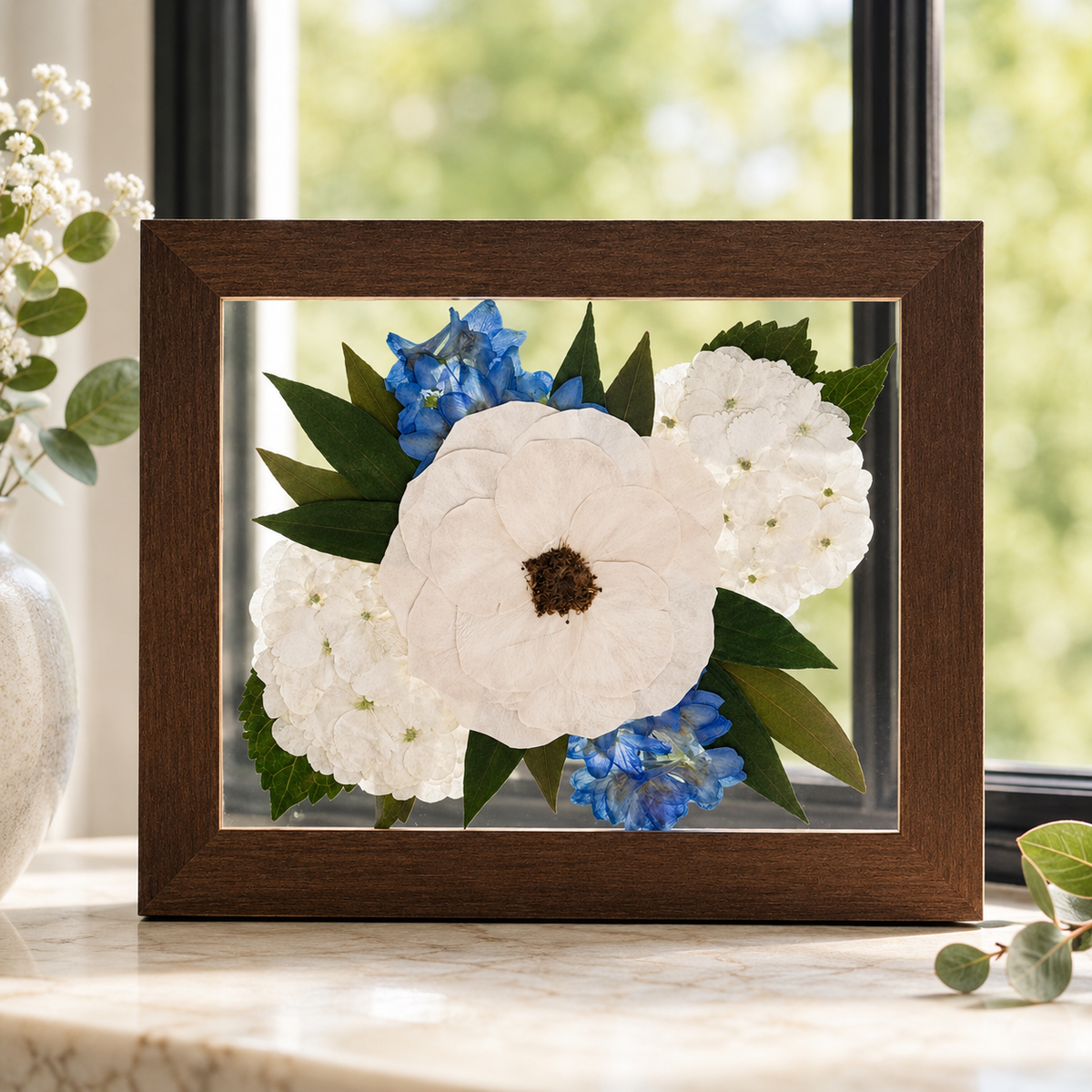 Pressed white hydrangeas and blue flowers with greenery preserved in a brown 8x10 frame.