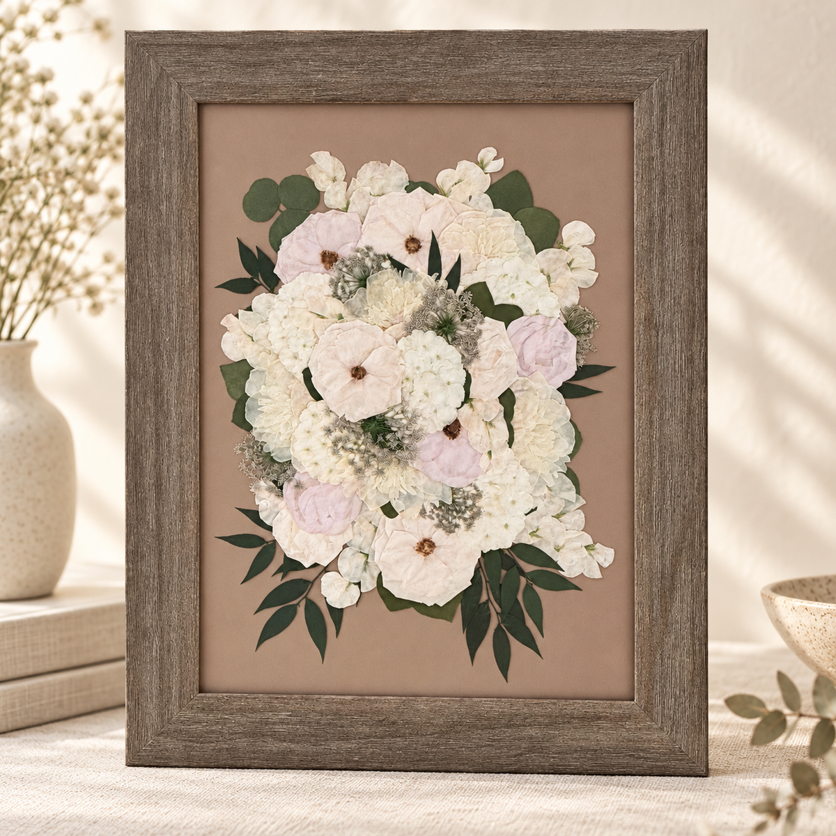 Full pressed bouquet with white and blush flowers and greenery preserved in a brown frame.