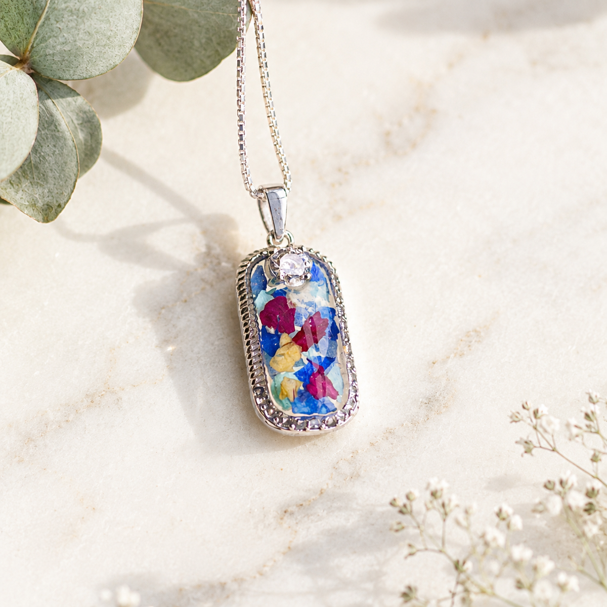 Graceful Remembrance Pendant with blue, pink, yellow and white preserved flowers.