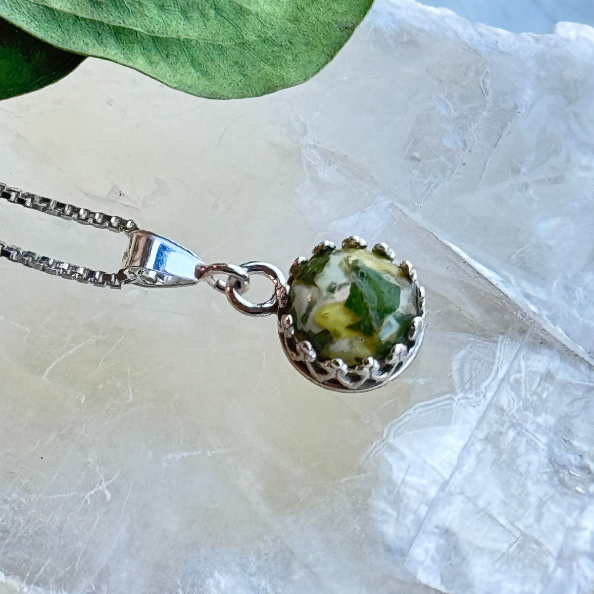 Close-up of green and white preserved flower resin pendant in sterling silver crown setting, handmade memory keepsake necklace
