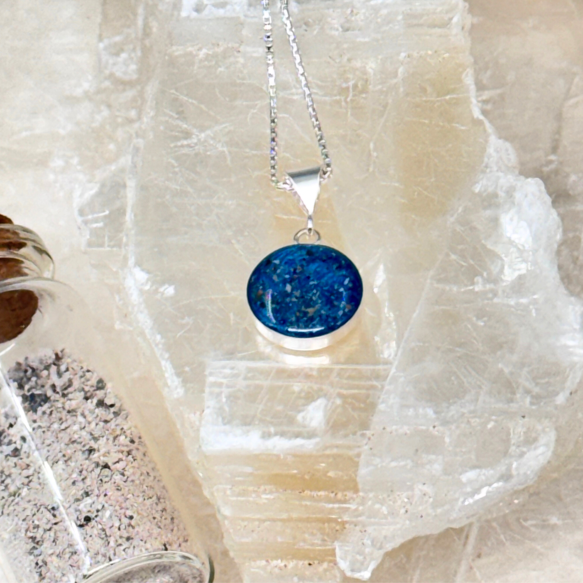Side view of the Loyal Companion pet ash pendant shown next to a small bottle of ashes, illustrating the materials used to create the memorial keepsake.