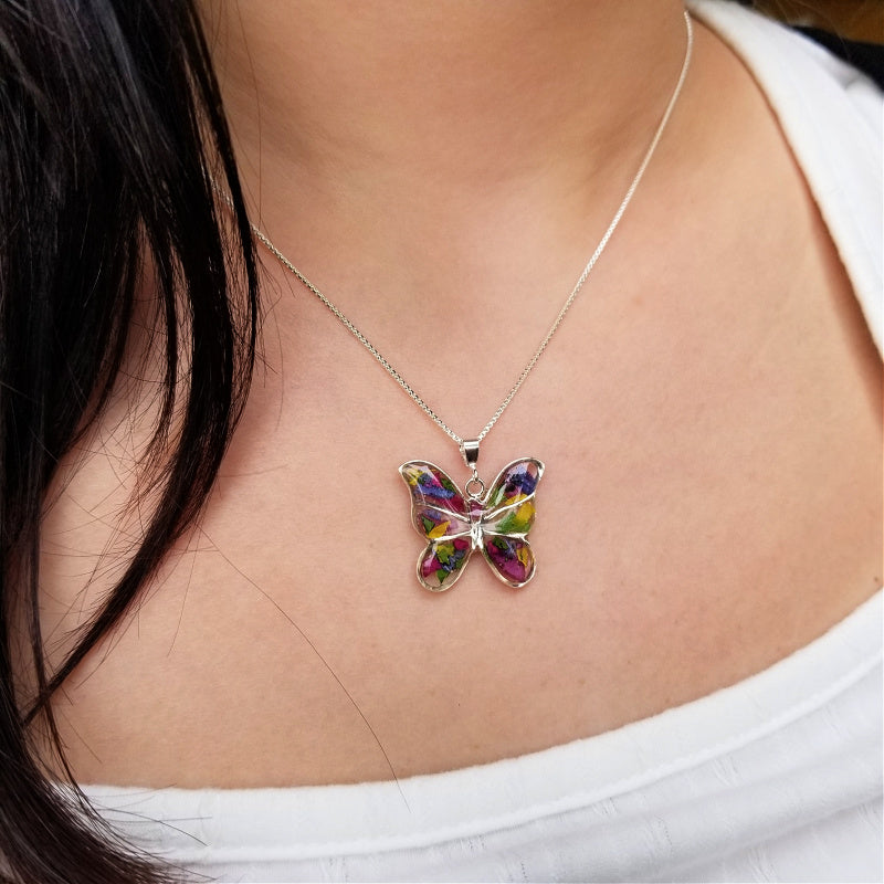 Model wearing a butterfly keepsake pendant with green, yellow, pink, and purple preserved flowers.0