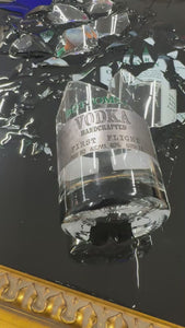 Luxury framed vodka bottle art featuring shattered glass, a black background, ornate gold frame, and personalized engraved nameplate commemorating a special occasion.