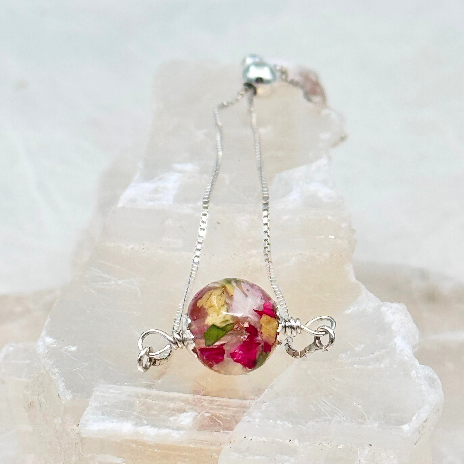 Custom resin bracelet with preserved pink, white, and yellow flower petals in a round bead on a sterling silver chain, shown without an initial charm.