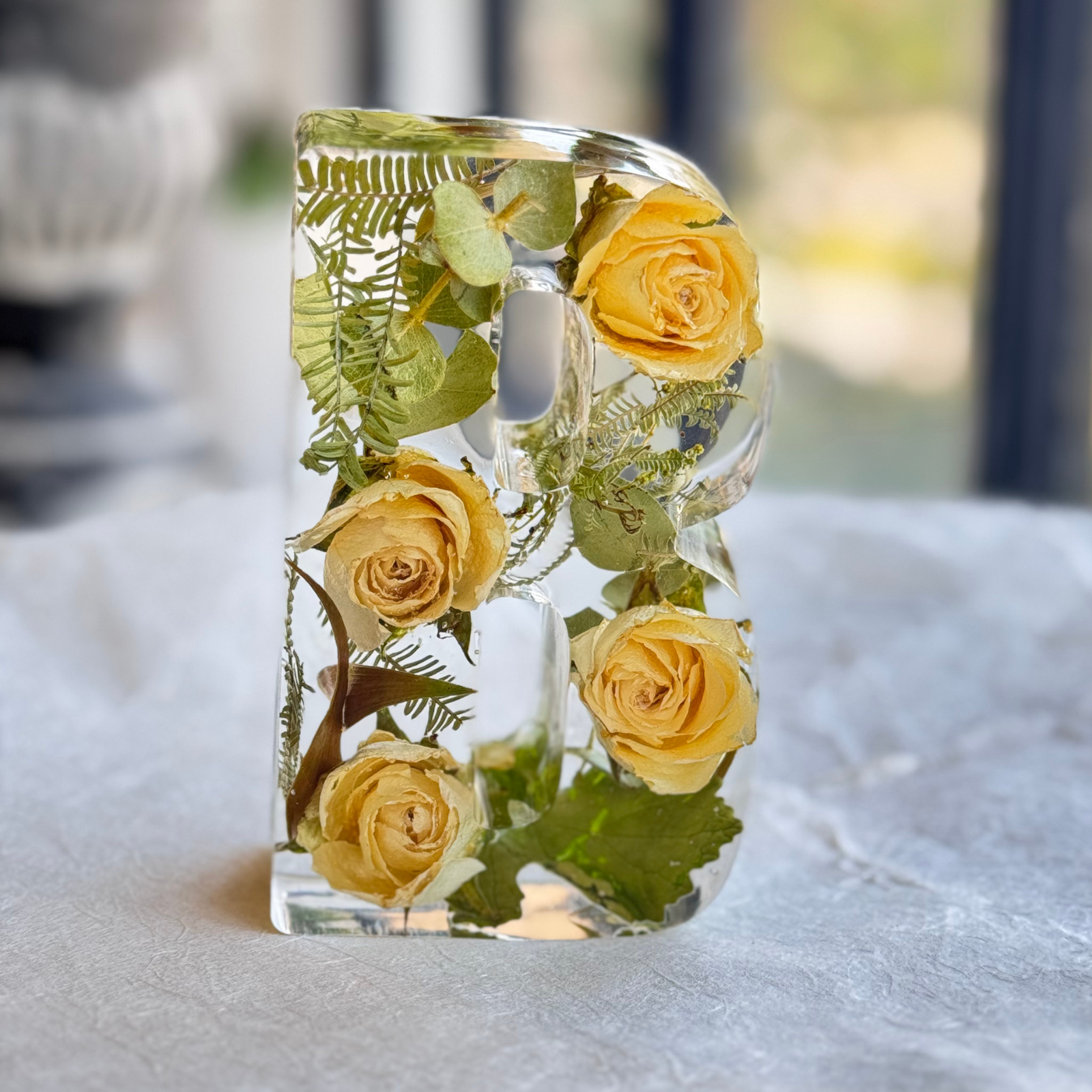 Resin letter “B” keepsake filled with preserved flower petals, shown in natural light for detail.