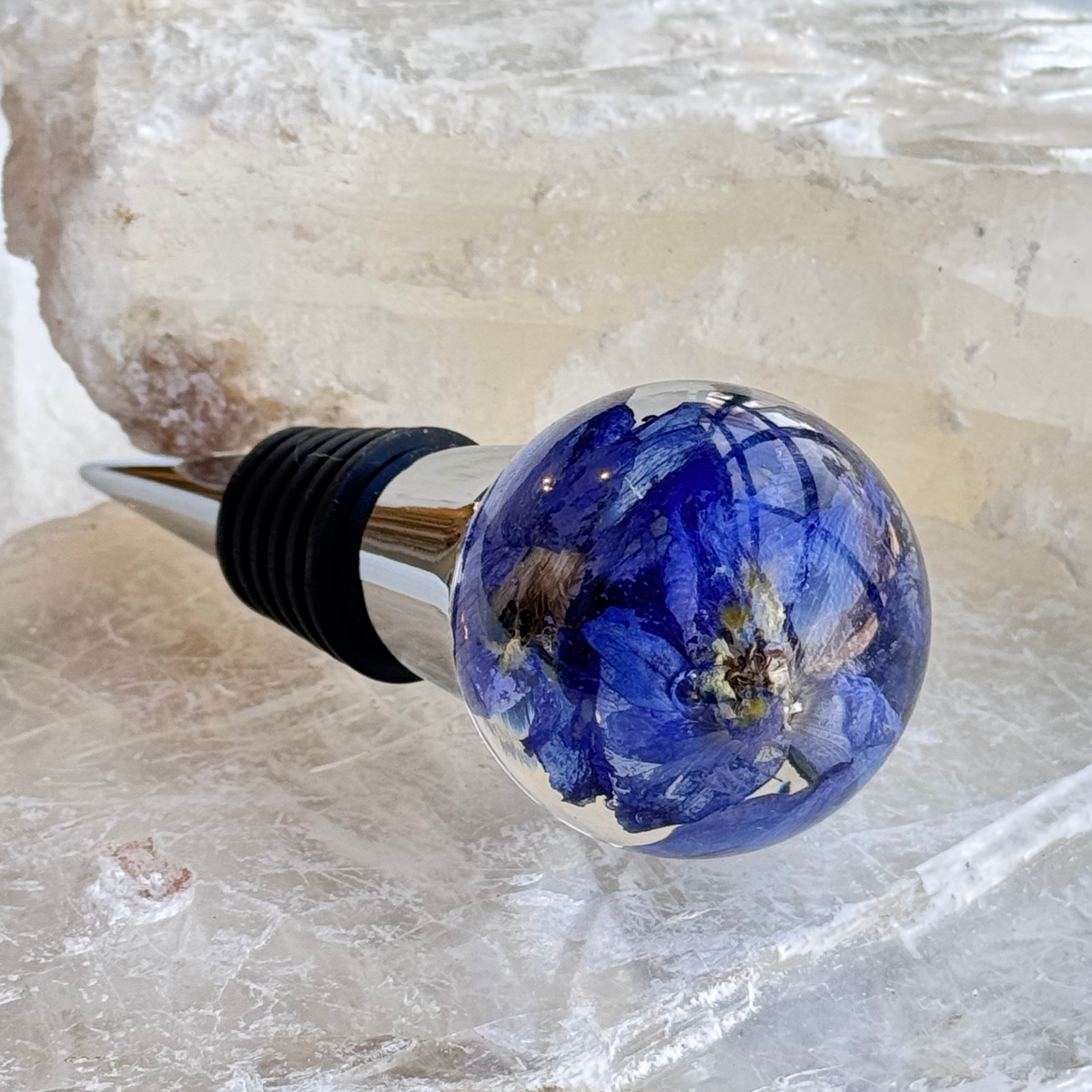Custom wine stopper handcrafted with preserved blue delphinium flowers in resin, a personalized floral keepsake for weddings or memorial events.