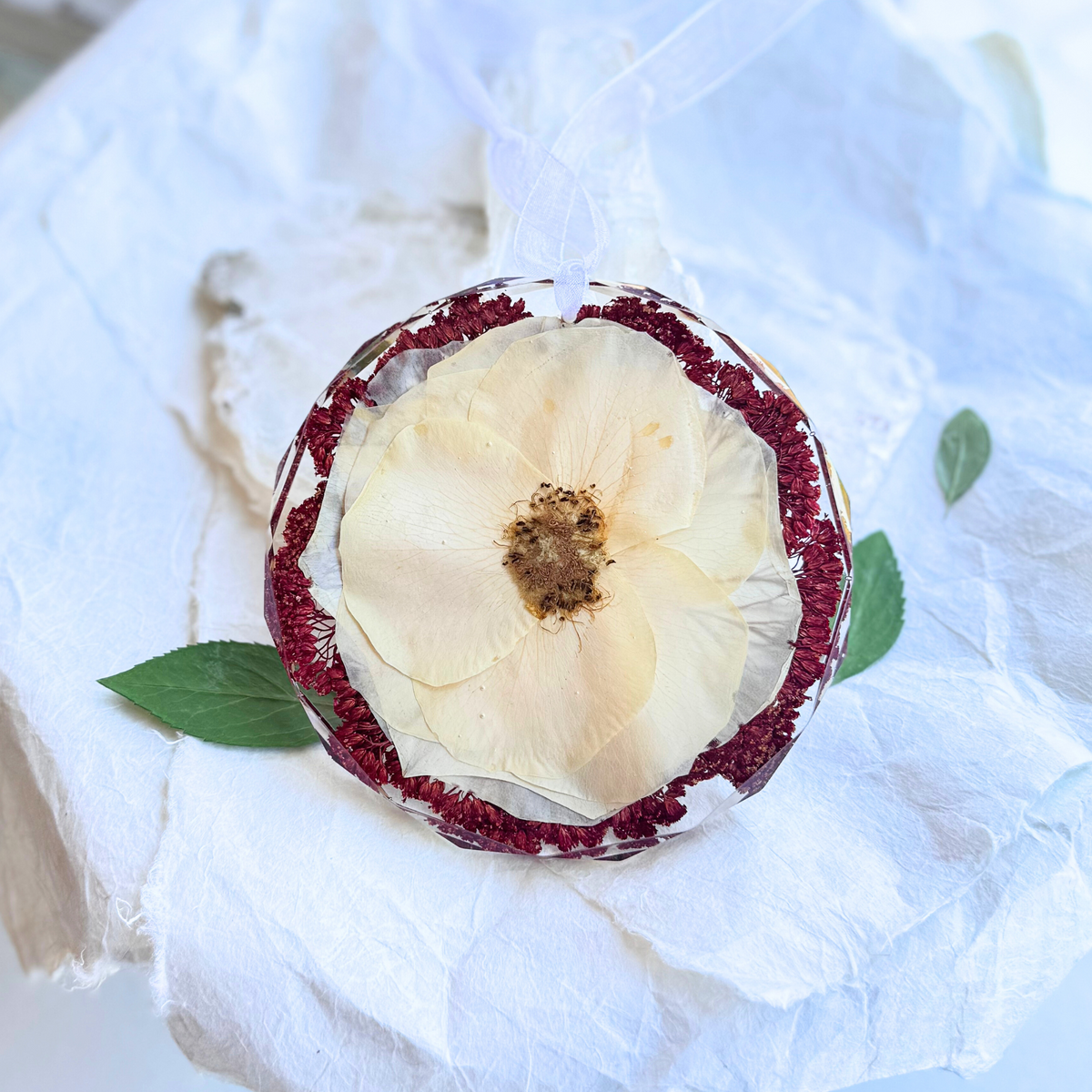 Round resin ornament with preserved white flower and red floral accents, handmade keepsake from wedding or funeral bouquet