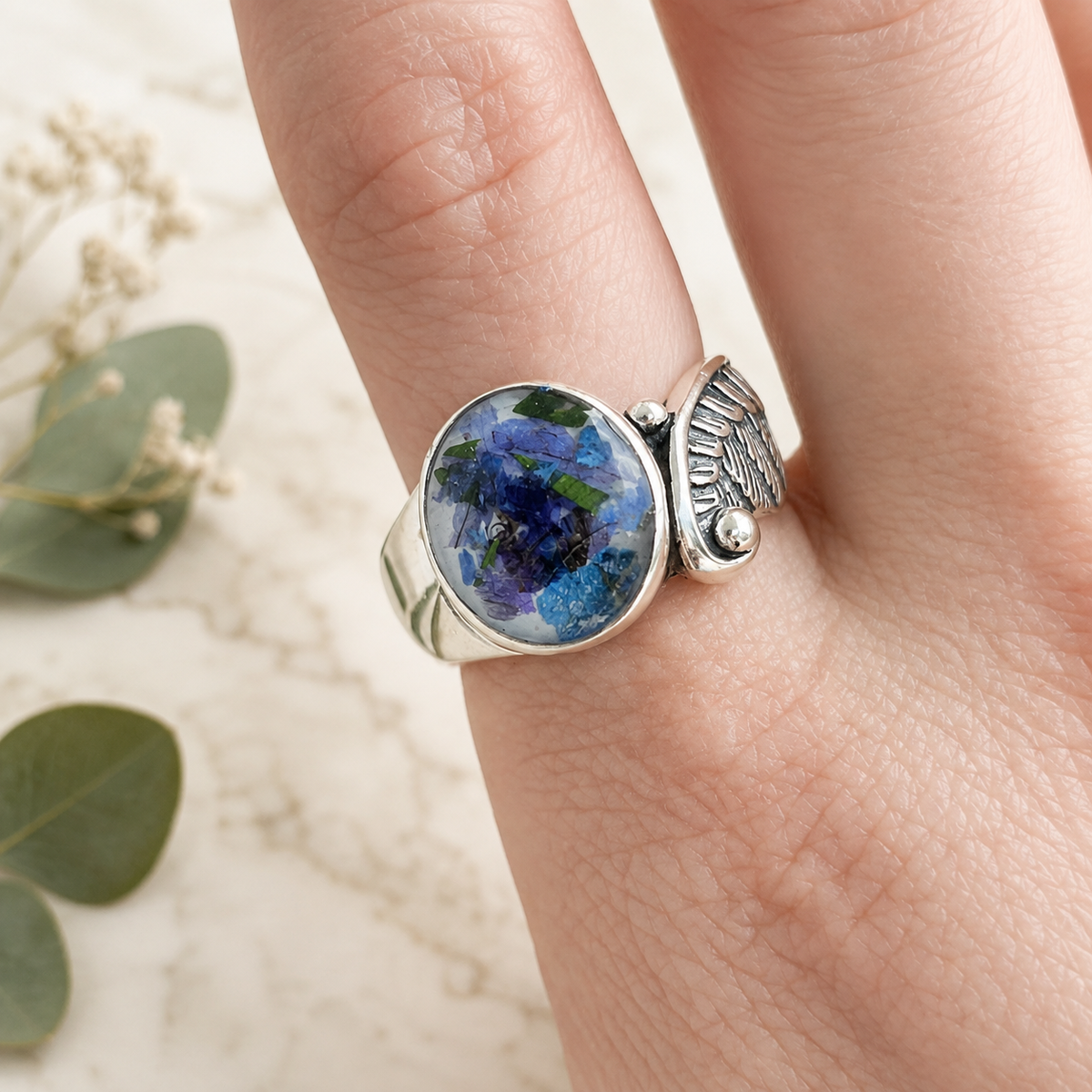 Model wearing Seraphina Memorial Ring with blue preserved flowers in a silver setting.