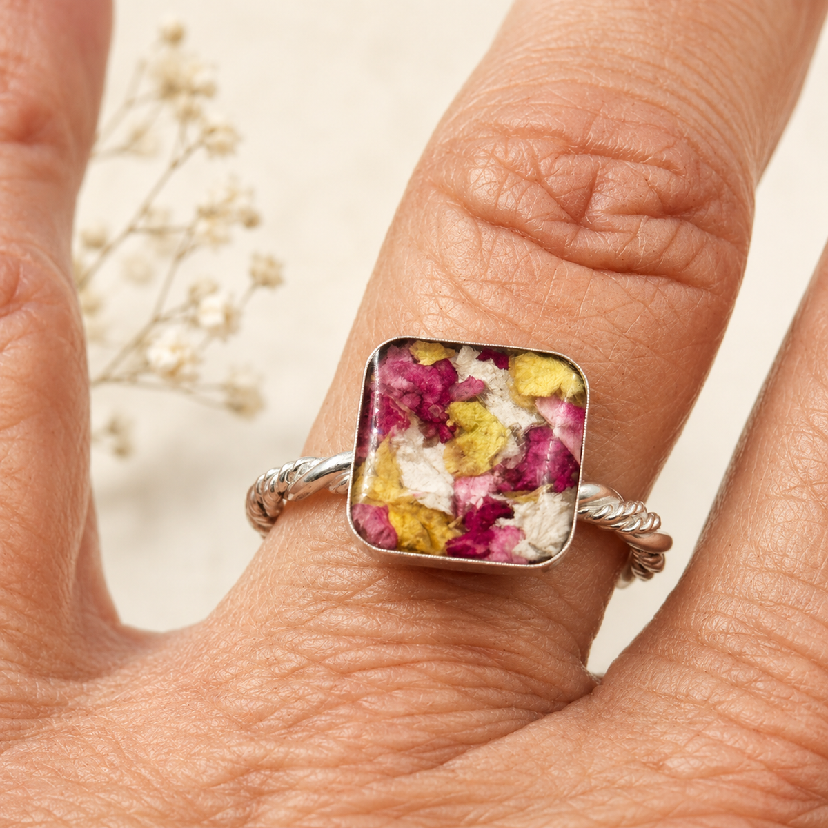 Square Memorial Flower Ring with pink, yellow and white preserved flowers shown on hand.