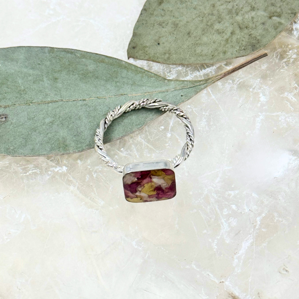 Side angle of sterling silver square memorial flower ring with preserved red, pink, and yellow funeral flowers set in resin and paired with a twisted band.