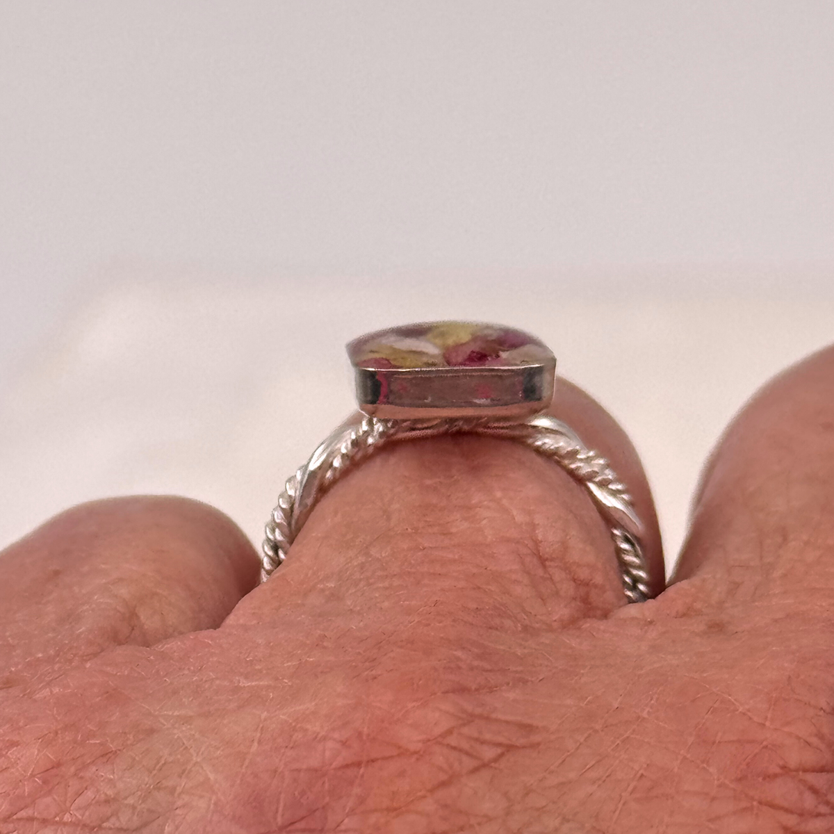 Side profile view of the sterling silver square memorial flower ring worn on a finger, showing the raised resin setting filled with preserved funeral flowers.
