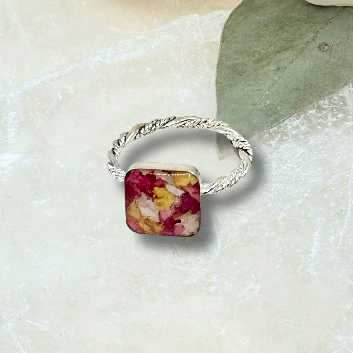 Sterling silver ring with square bezel filled with preserved memorial flowers in pink, red, and yellow tones. A meaningful keepsake made from funeral flowers.