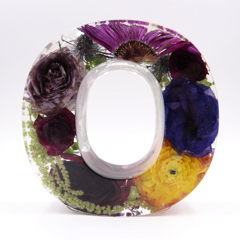 Resin letter O filled with preserved purple and yellow flowers from wedding or funeral bouquet, vibrant floral keepsake
