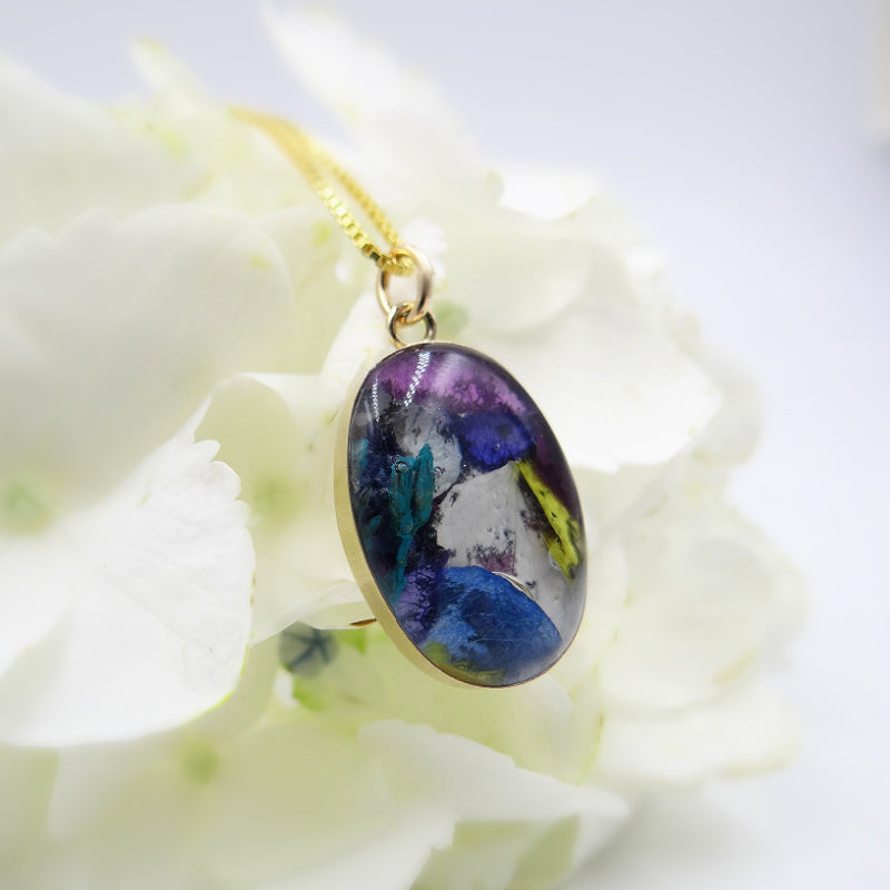 A gold-filled oval memorial pendant infused with assorted preserved flowers, creating a unique and personal remembrance piece.