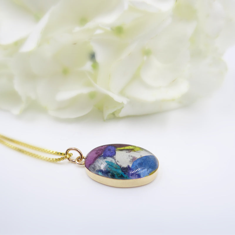 A side view of the Gold Timeless Floral Keepsake pendant, highlighting its gold-filled setting and floral inlay with assorted preserved flowers.
