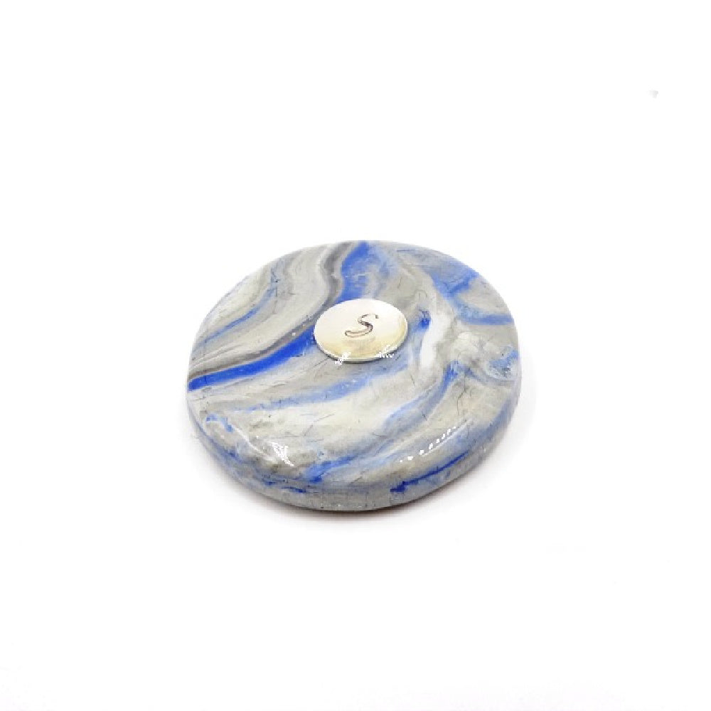 A close-up view of a custom pet memorial golf ball marker, handcrafted with pet ashes or fur. Features a smooth, glossy finish with personalized colors and an engraved initial.